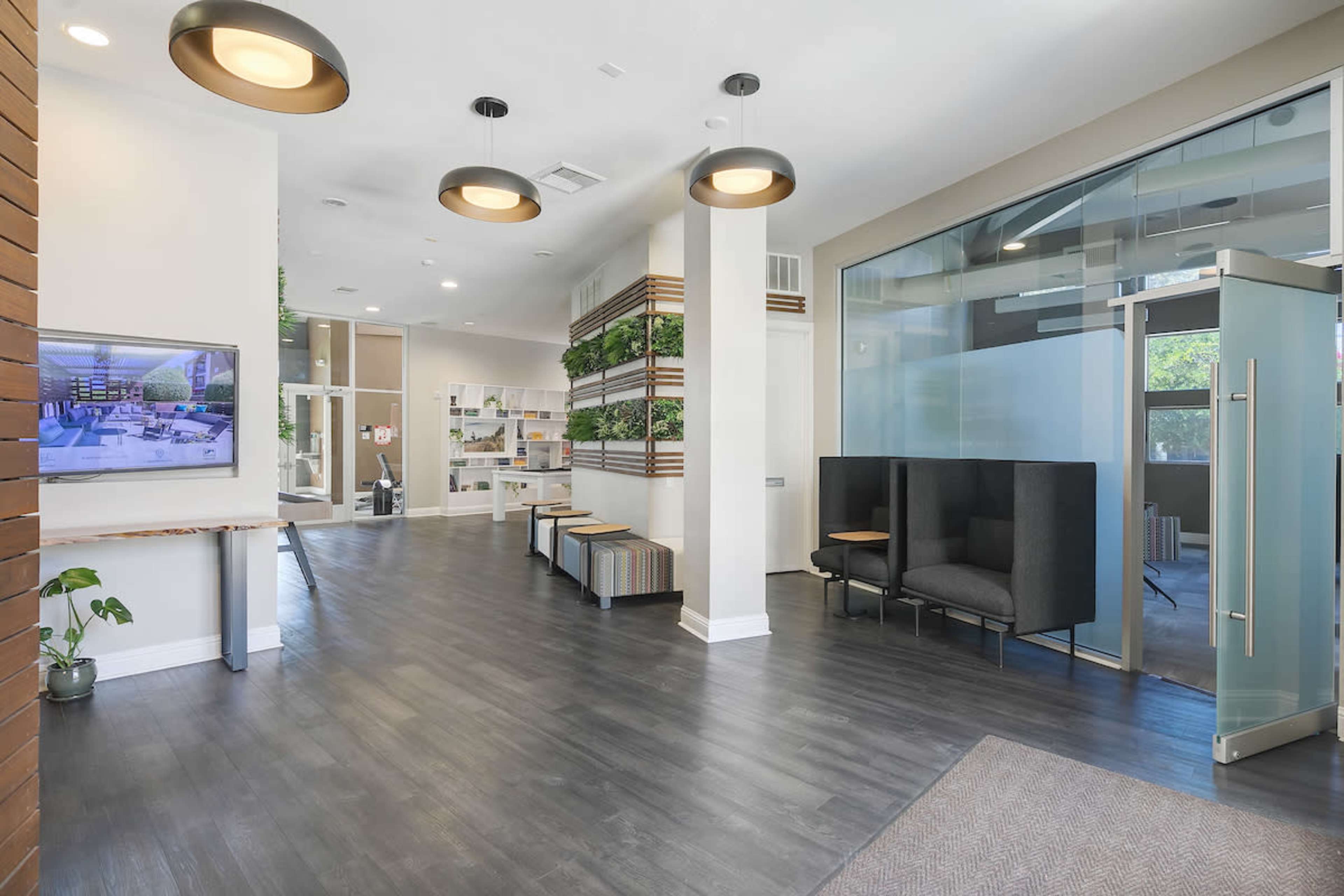 The image shows a modern reception area with seating, greenery, and a digital screen displaying images on one wall.
