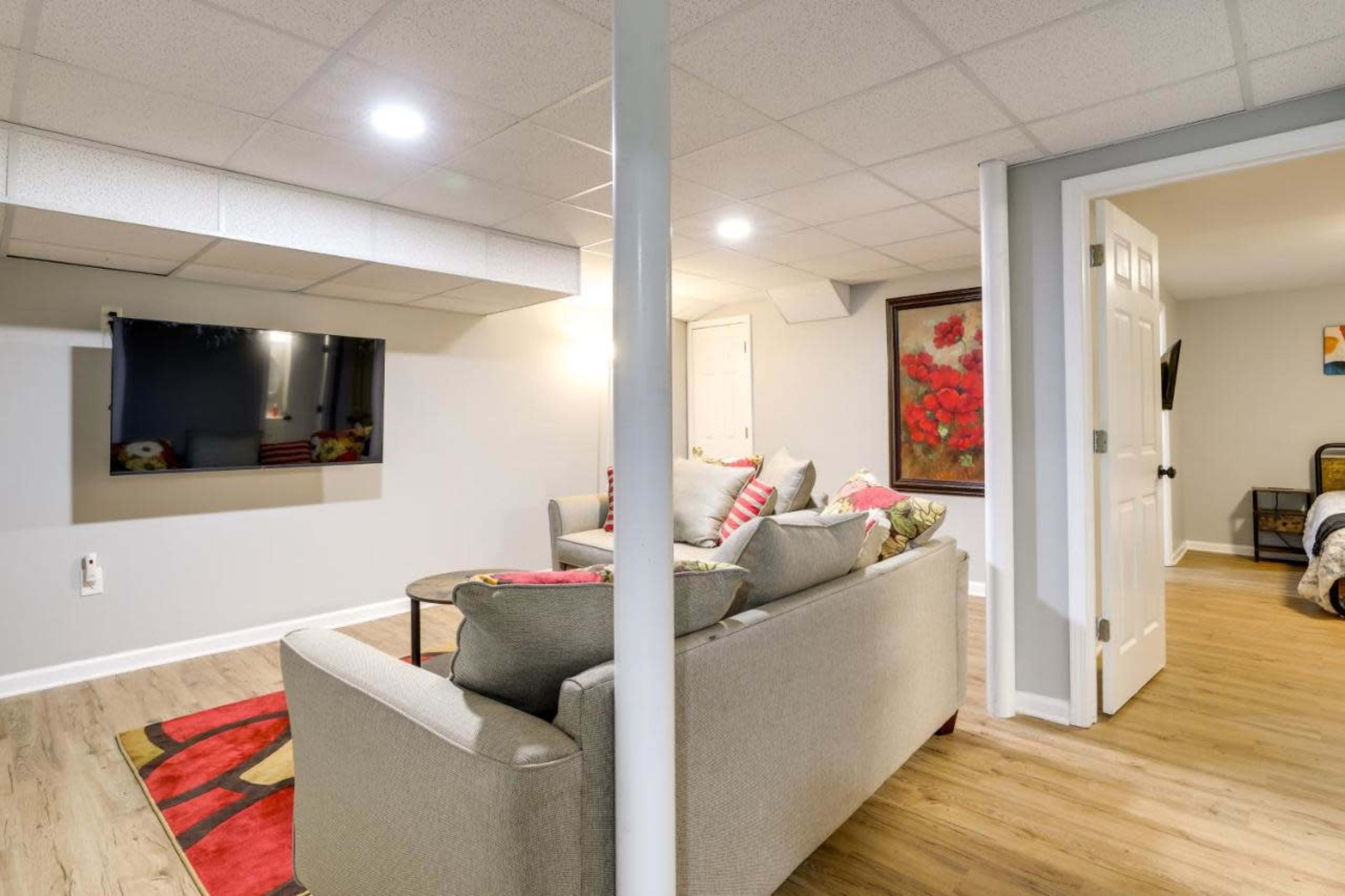 The image shows a basement living area with a couch, a TV mounted on the wall, and a doorway leading to another room.