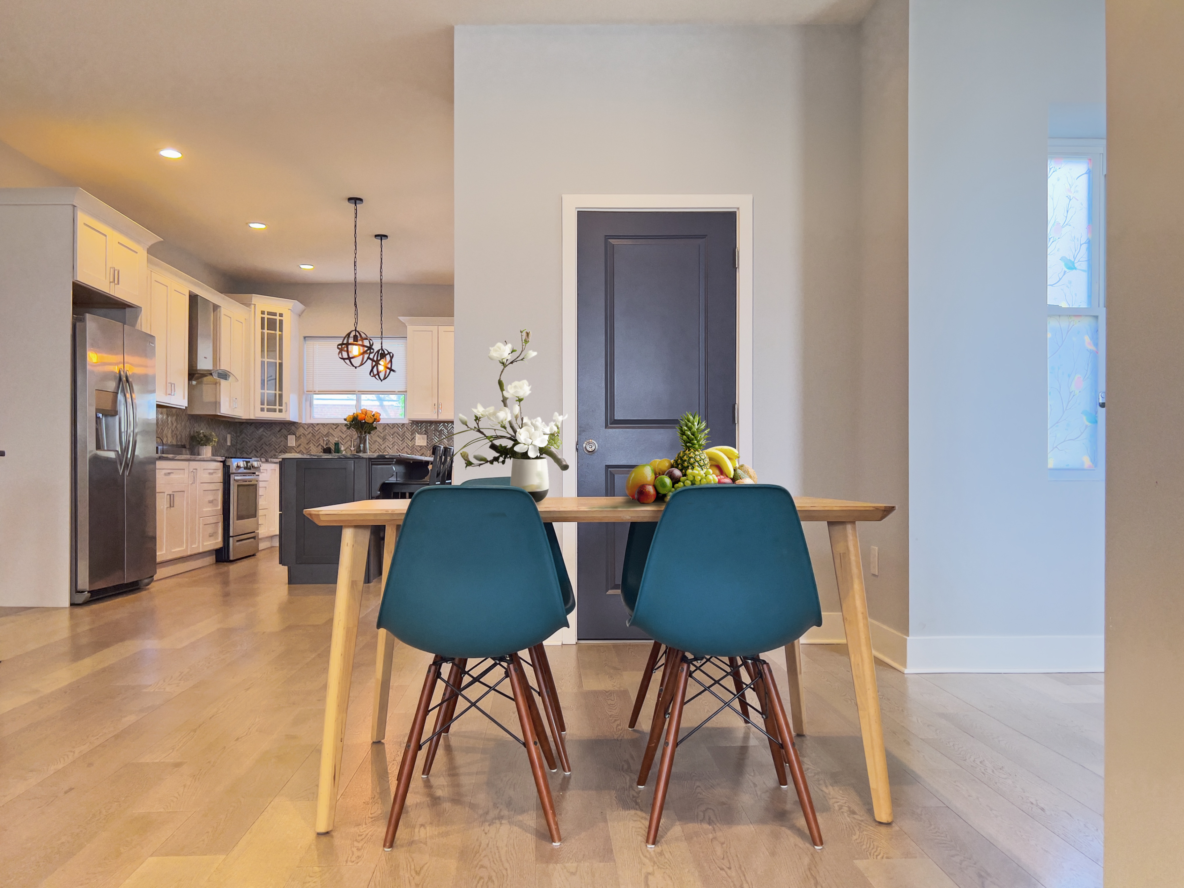 A dining table with blue chairs is positioned near a kitchen featuring white cabinetry and stainless steel appliances.