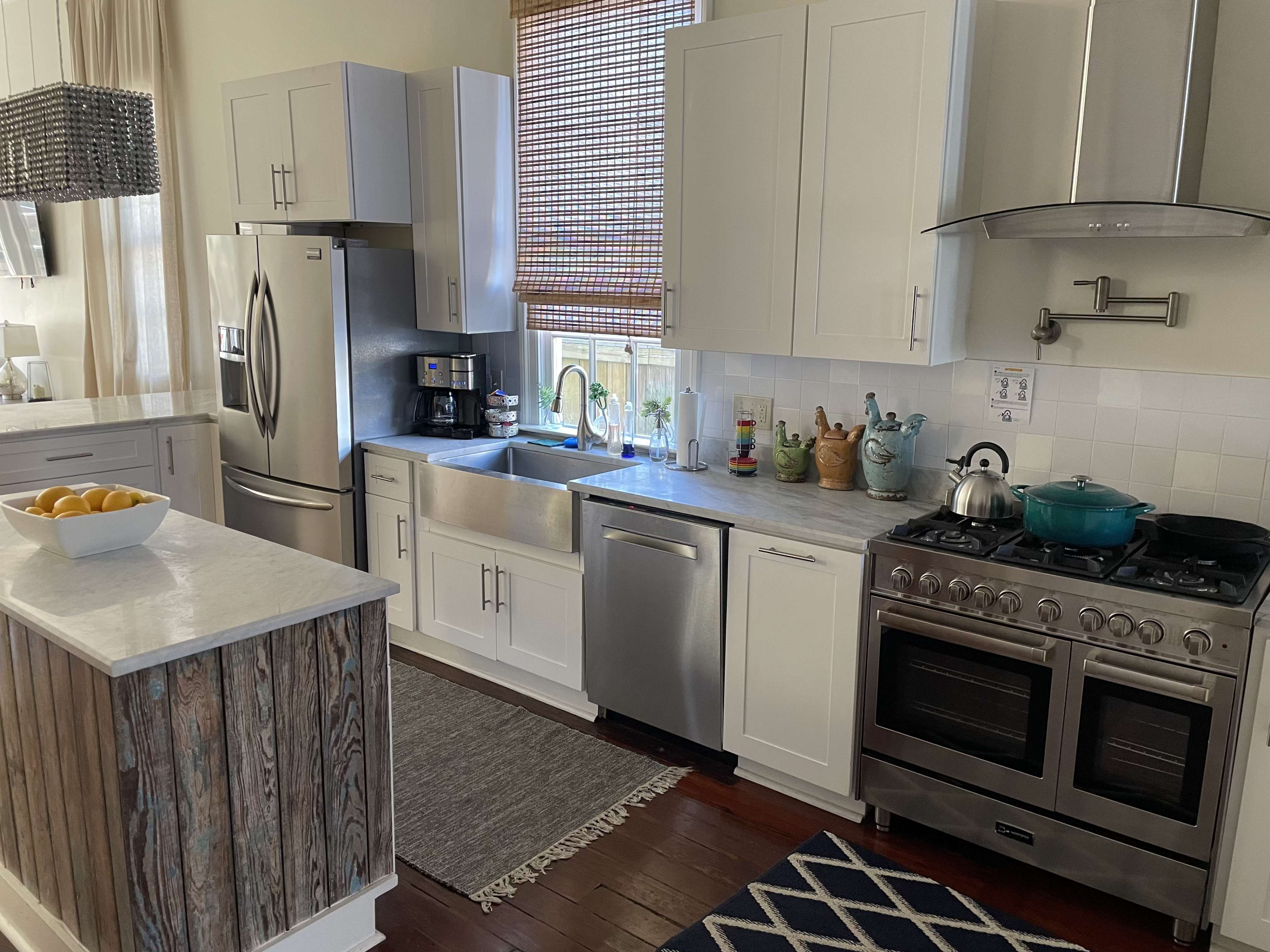 A modern kitchen with stainless steel appliances, white cabinets, a marble countertop, and a mix of wooden and tile flooring.