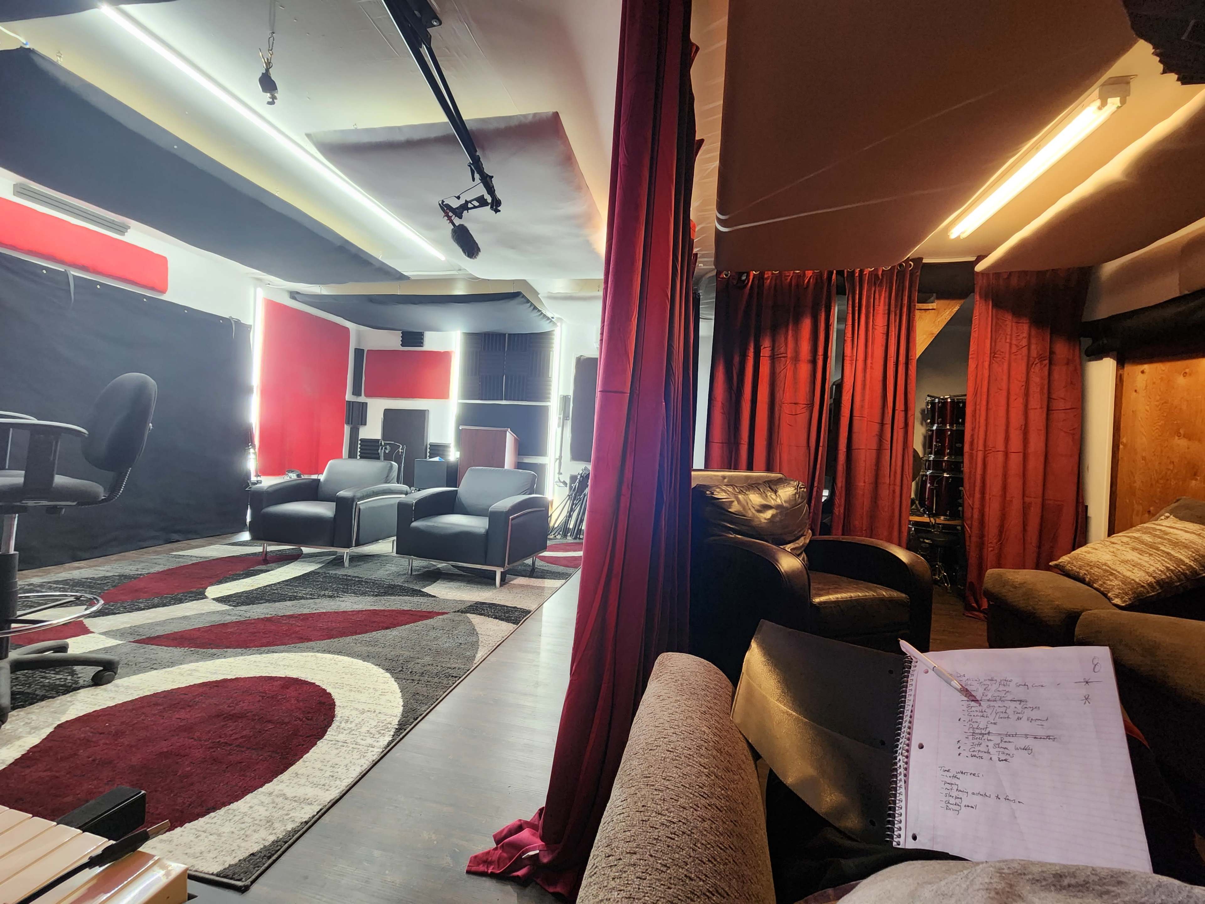 A recording studio with two seating areas, red curtains, sound panels, and a notebook on a couch.