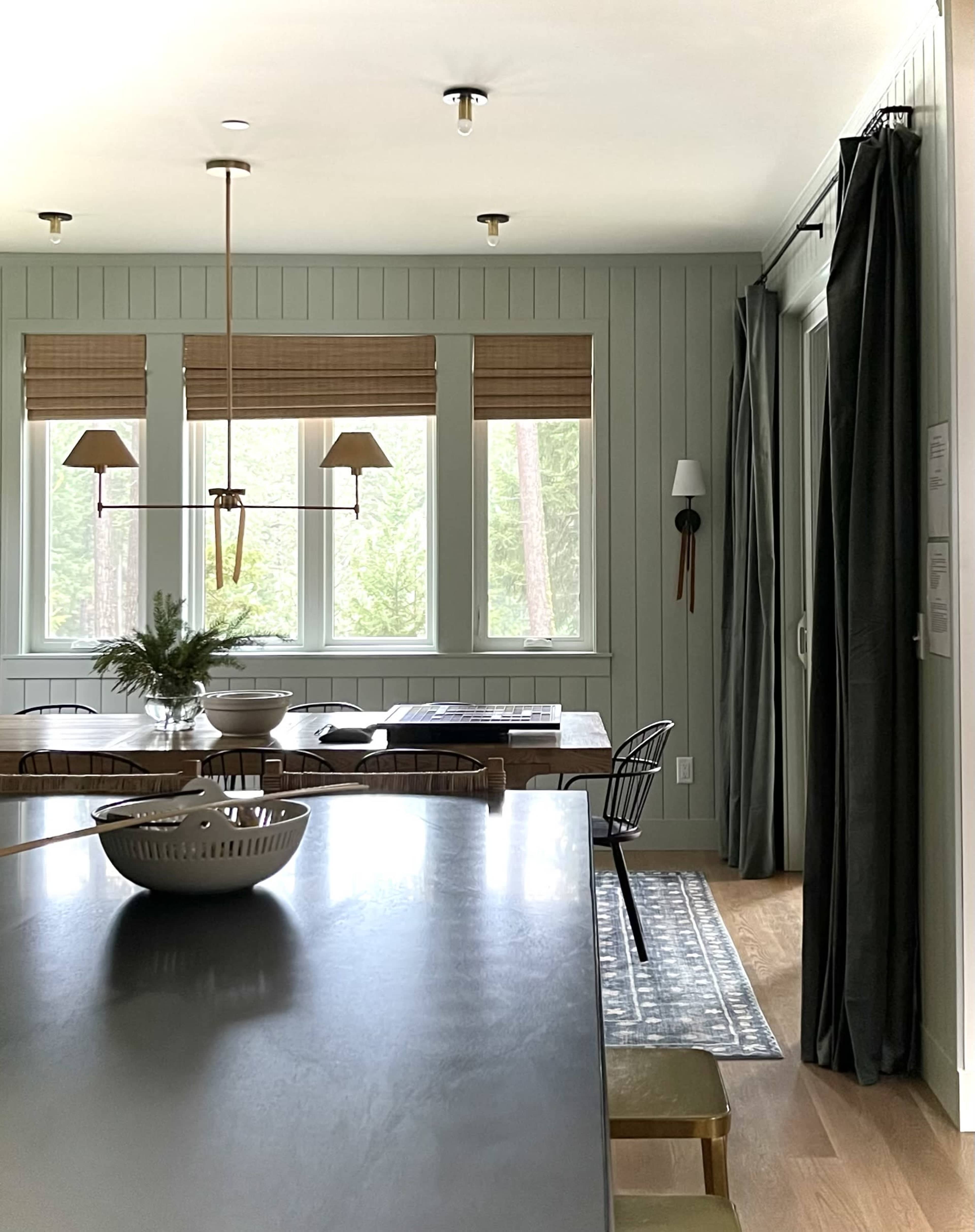 A modern dining area features a long wooden table, minimalist decor, and large windows with natural light filtering through.