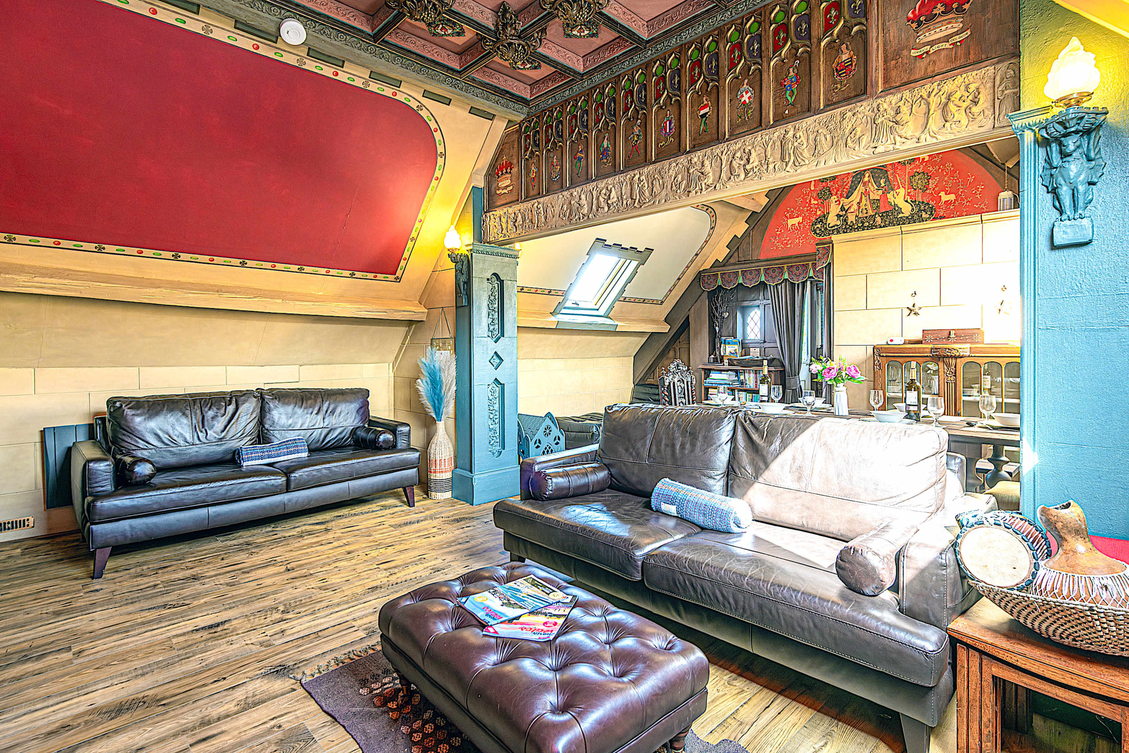 The image shows a cozy living room with leather sofas, wooden flooring, and ornate wall decorations, including a red accent wall and various artistic elements.