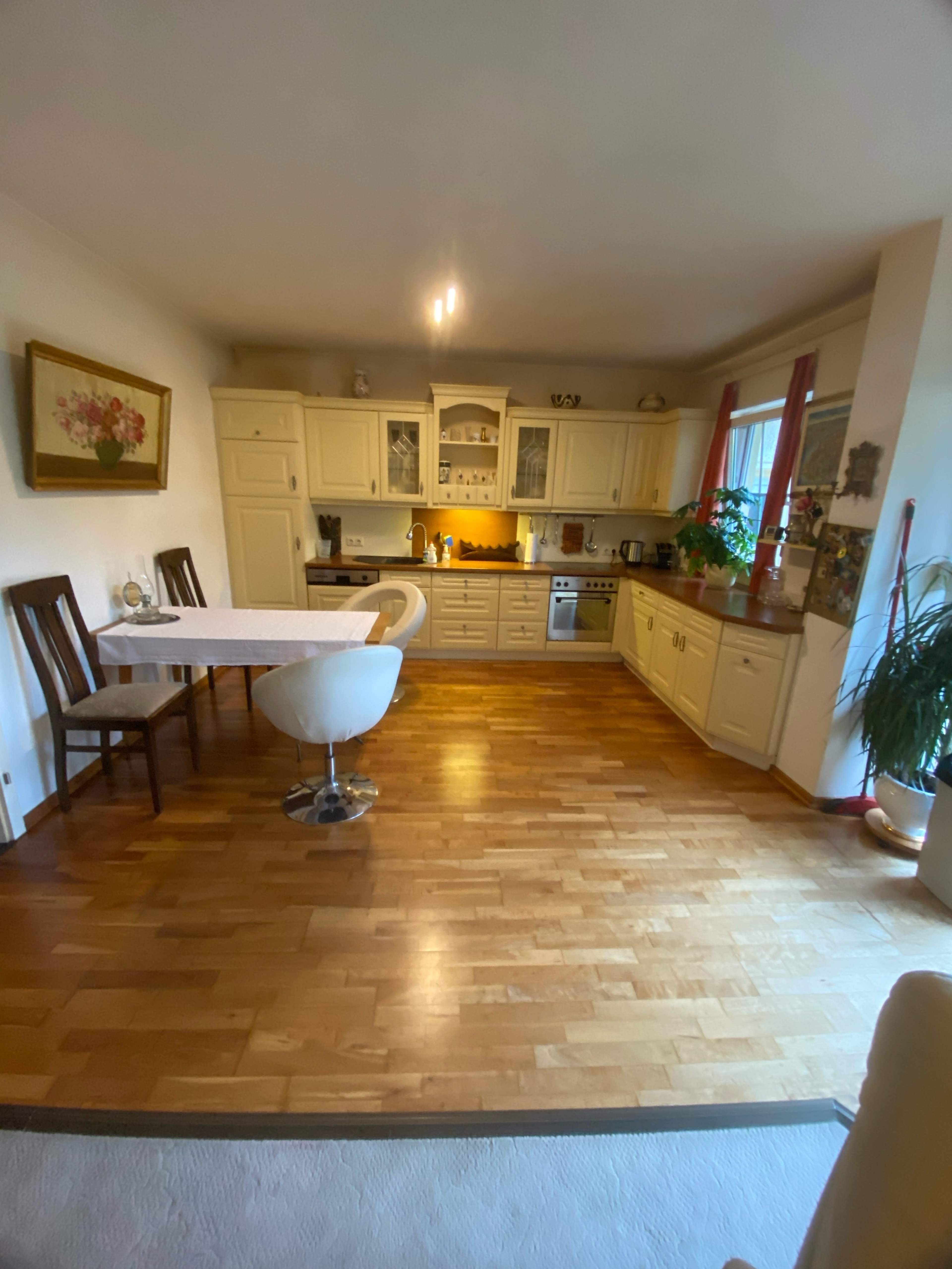 The image shows a modern kitchen with white cabinets, a dining table, and hardwood flooring.