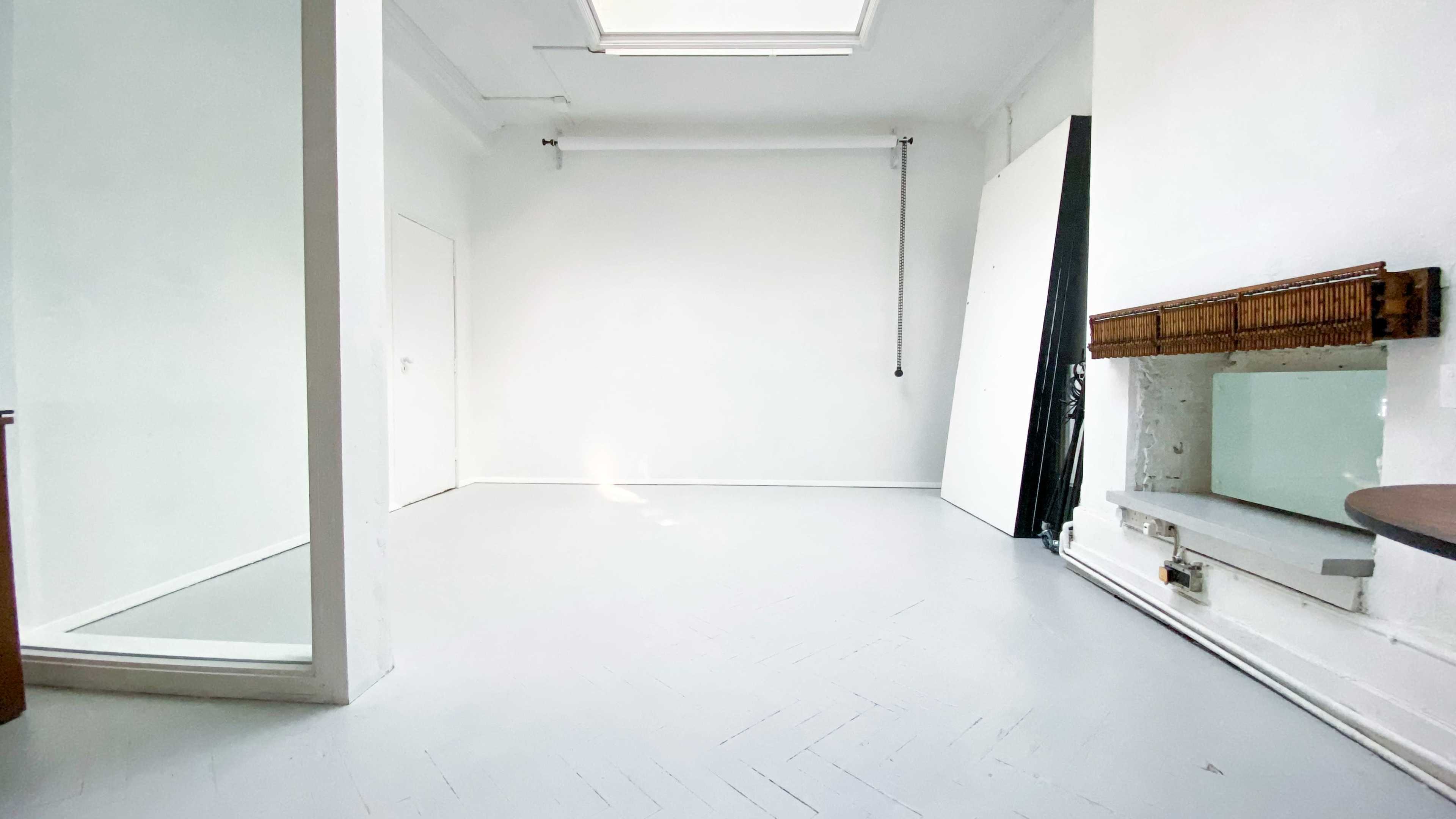 A bright, empty room with white walls, a skylight, and a large mirror on one side.
