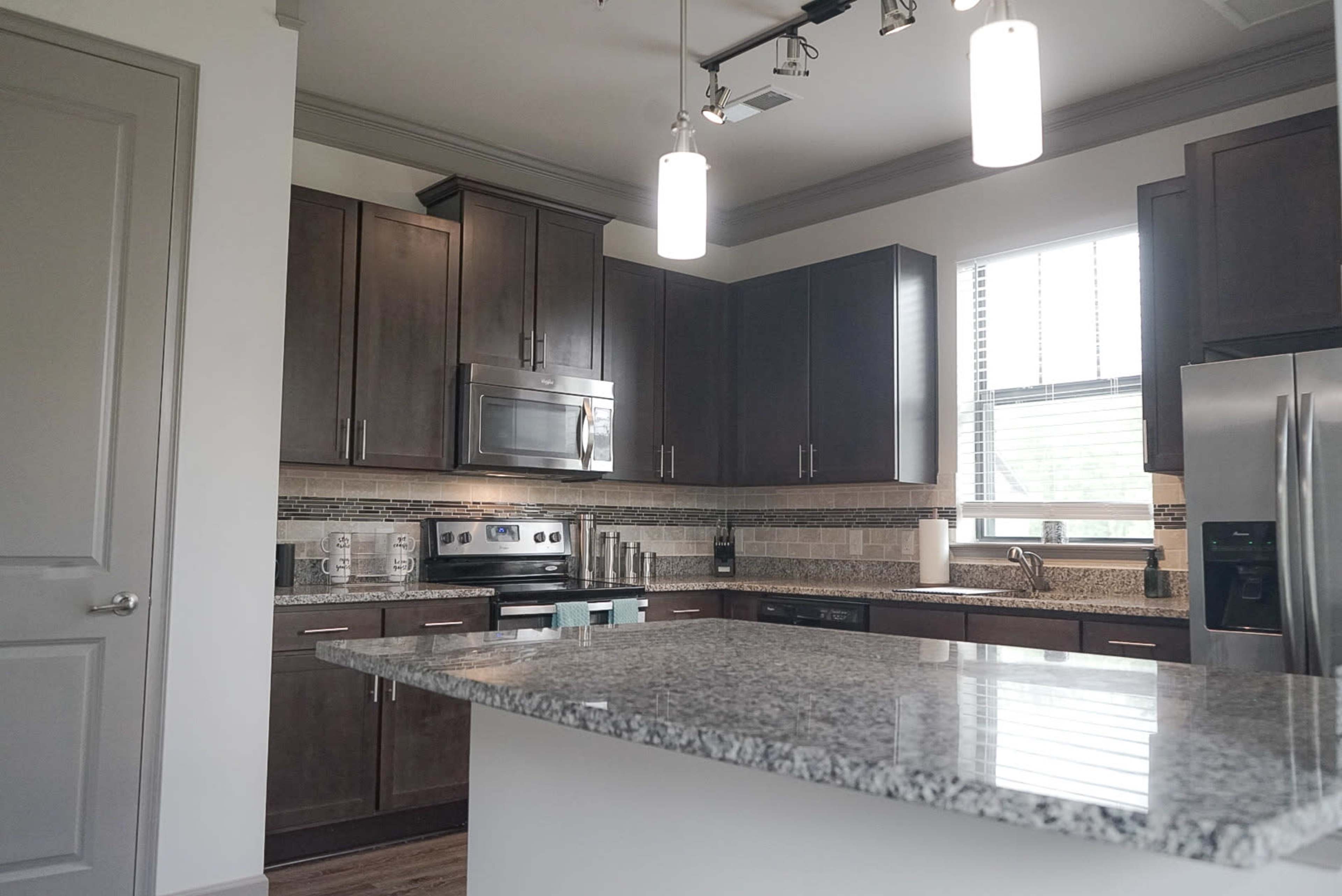 A modern kitchen featuring dark wooden cabinets, stainless steel appliances, and a granite countertop with bar seating.