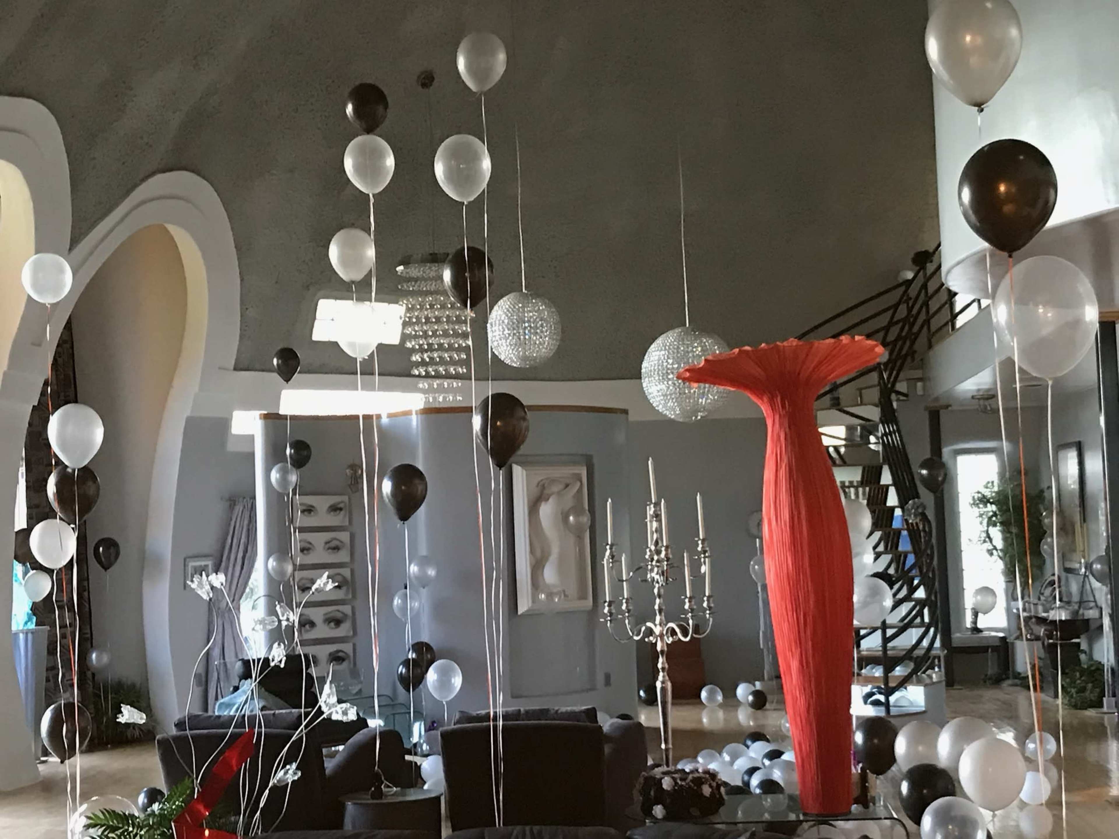 A modern living room decorated with black and white balloons, a red vase, and a chandelier.