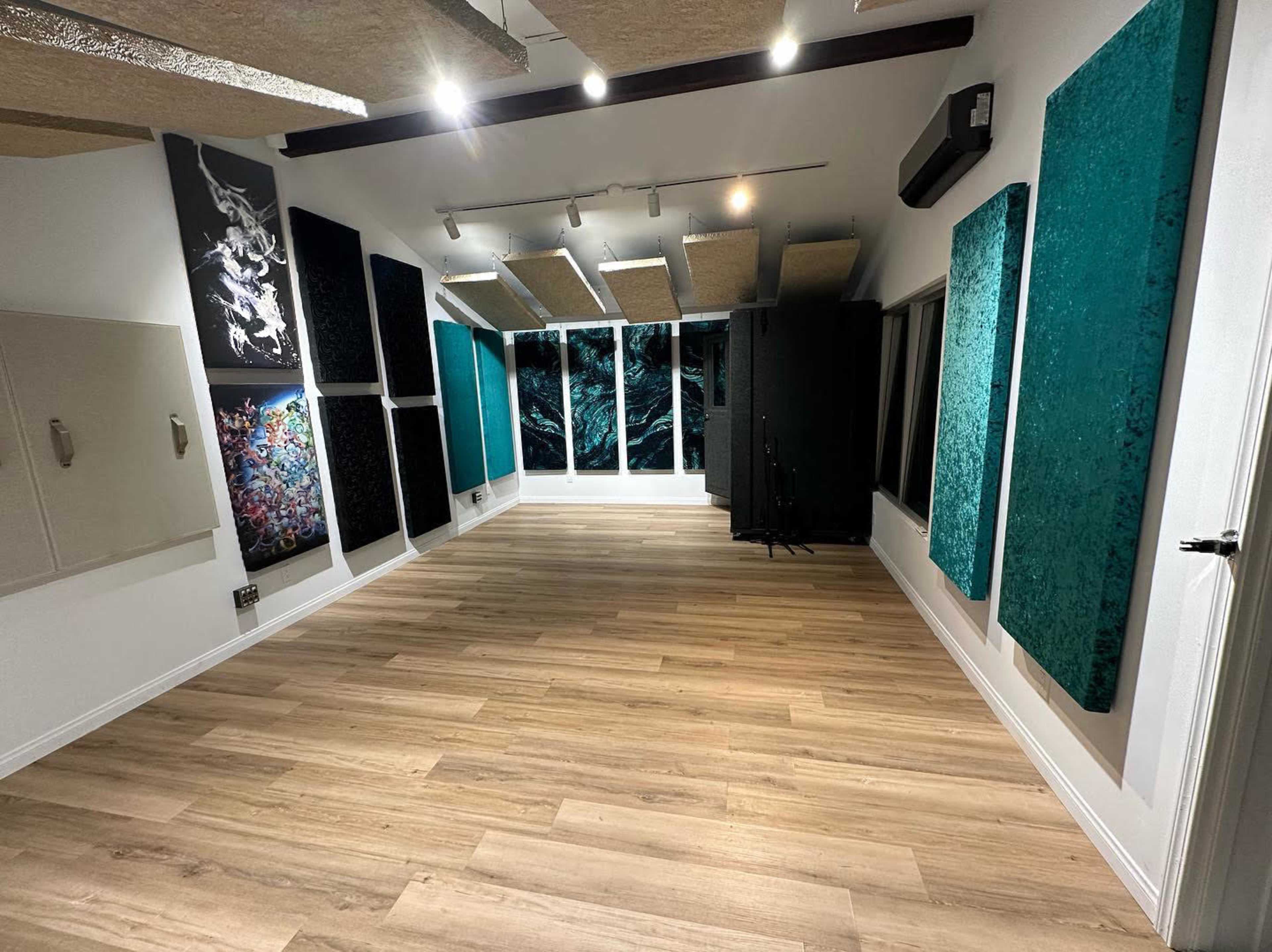 A soundproof recording studio with acoustic panels on the walls, wooden flooring, and large windows allowing natural light.