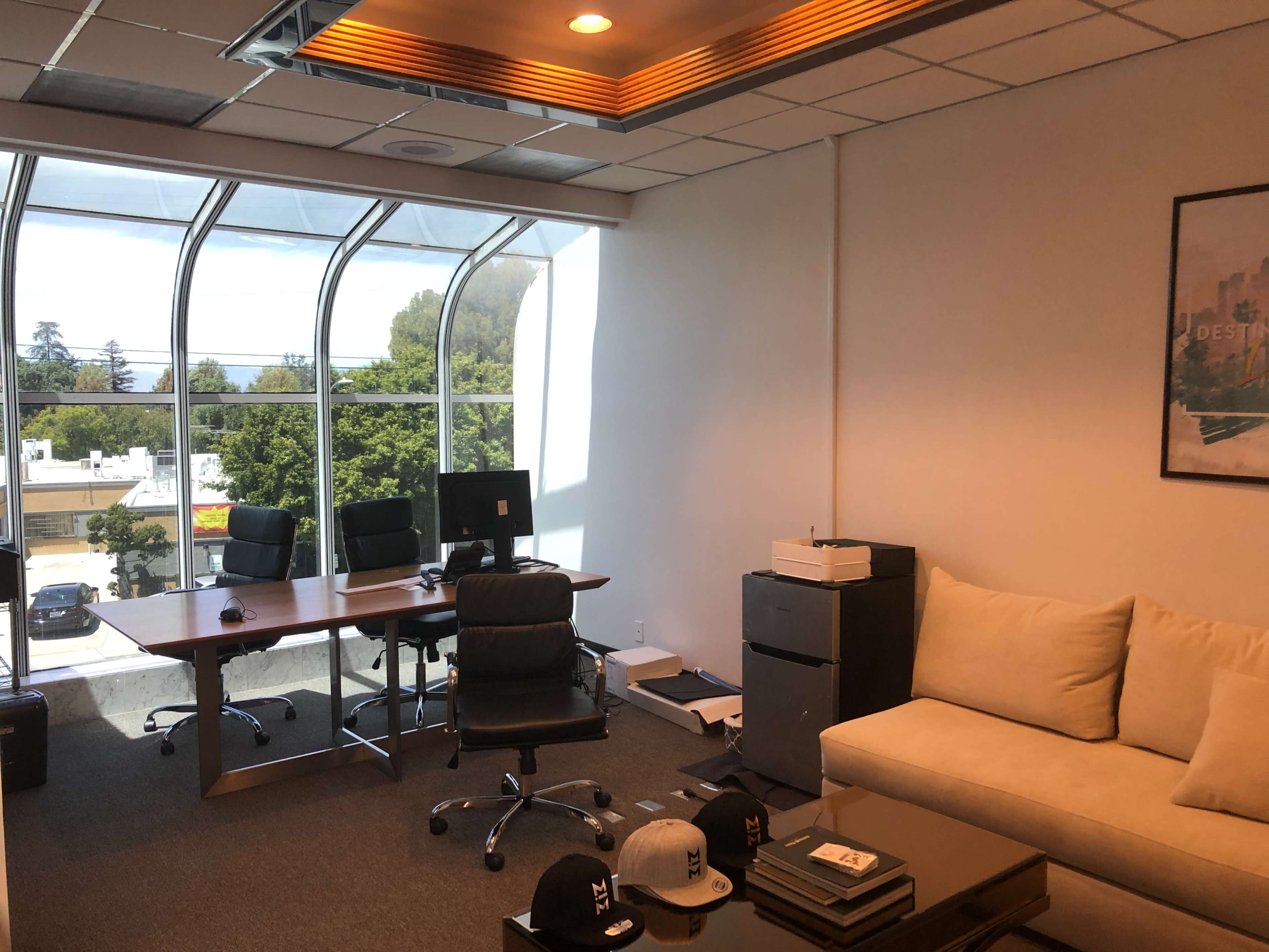 An office space featuring a sofa, two desks with computer monitors, and a filing cabinet, illuminated by natural light from large windows.