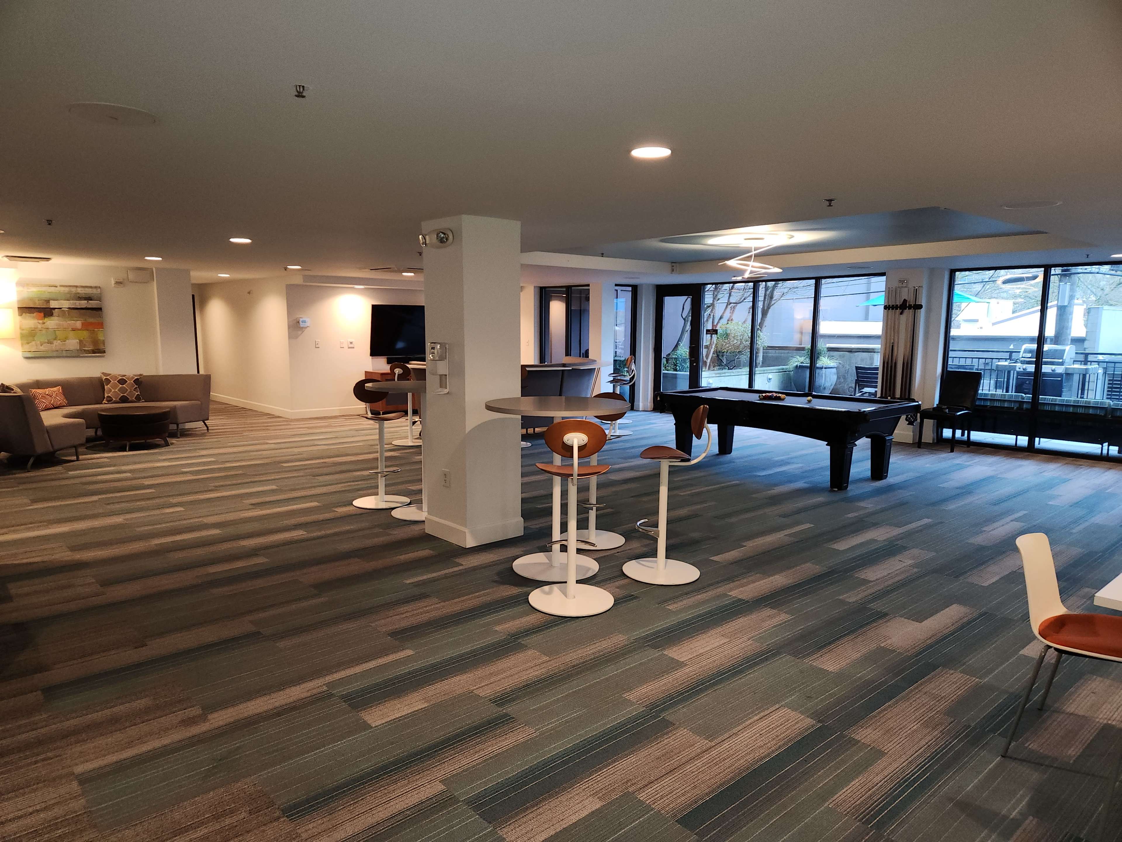 A modern lounge area featuring a pool table, seating arrangements, and large windows allowing natural light.