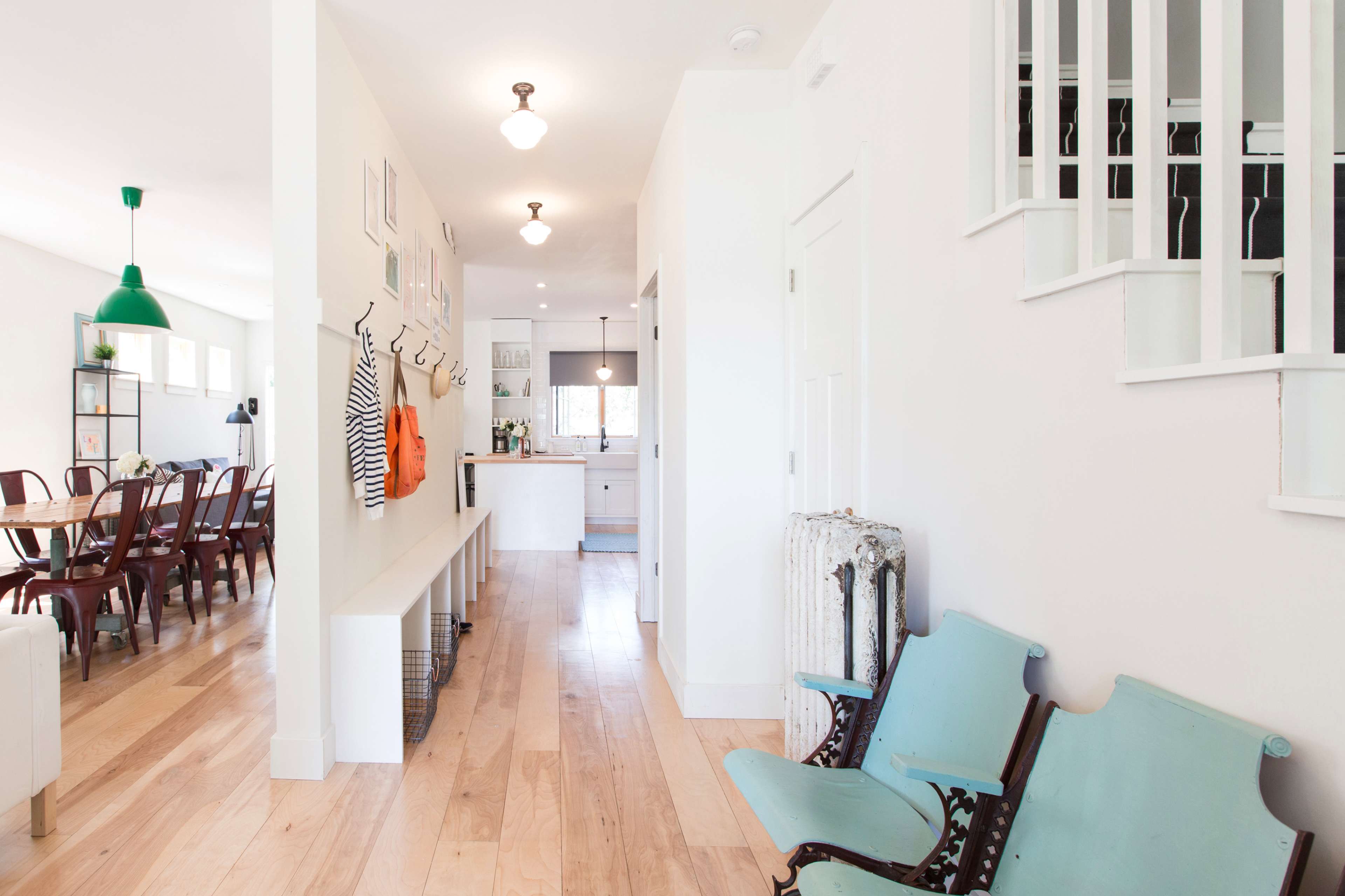 A bright, open hallway leading to a modern kitchen and dining area, with wooden floors and a seating area featuring vintage-looking chairs.