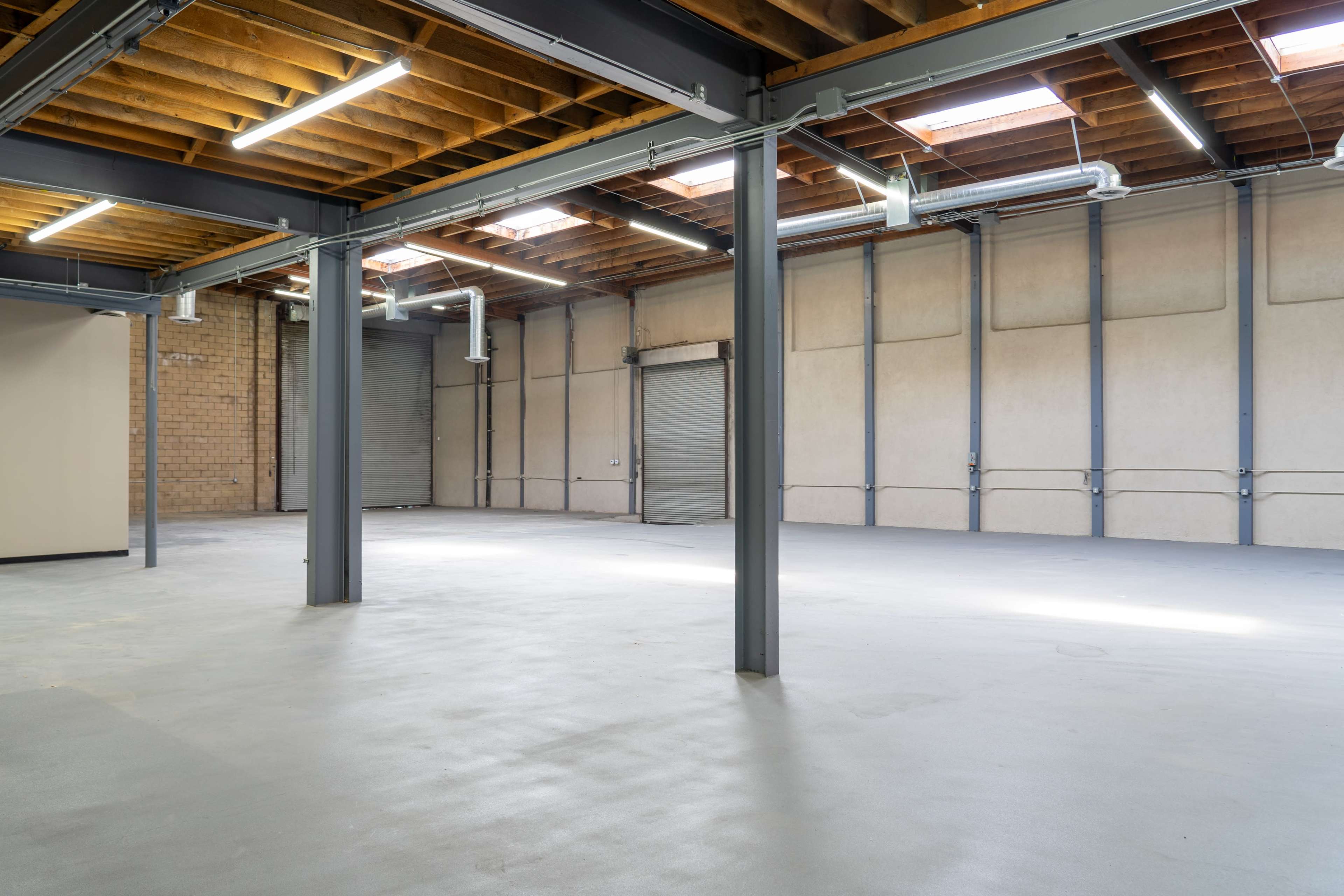 The image shows a spacious industrial interior with exposed wooden beams and metal pillars, featuring polished concrete flooring and large vacant areas.