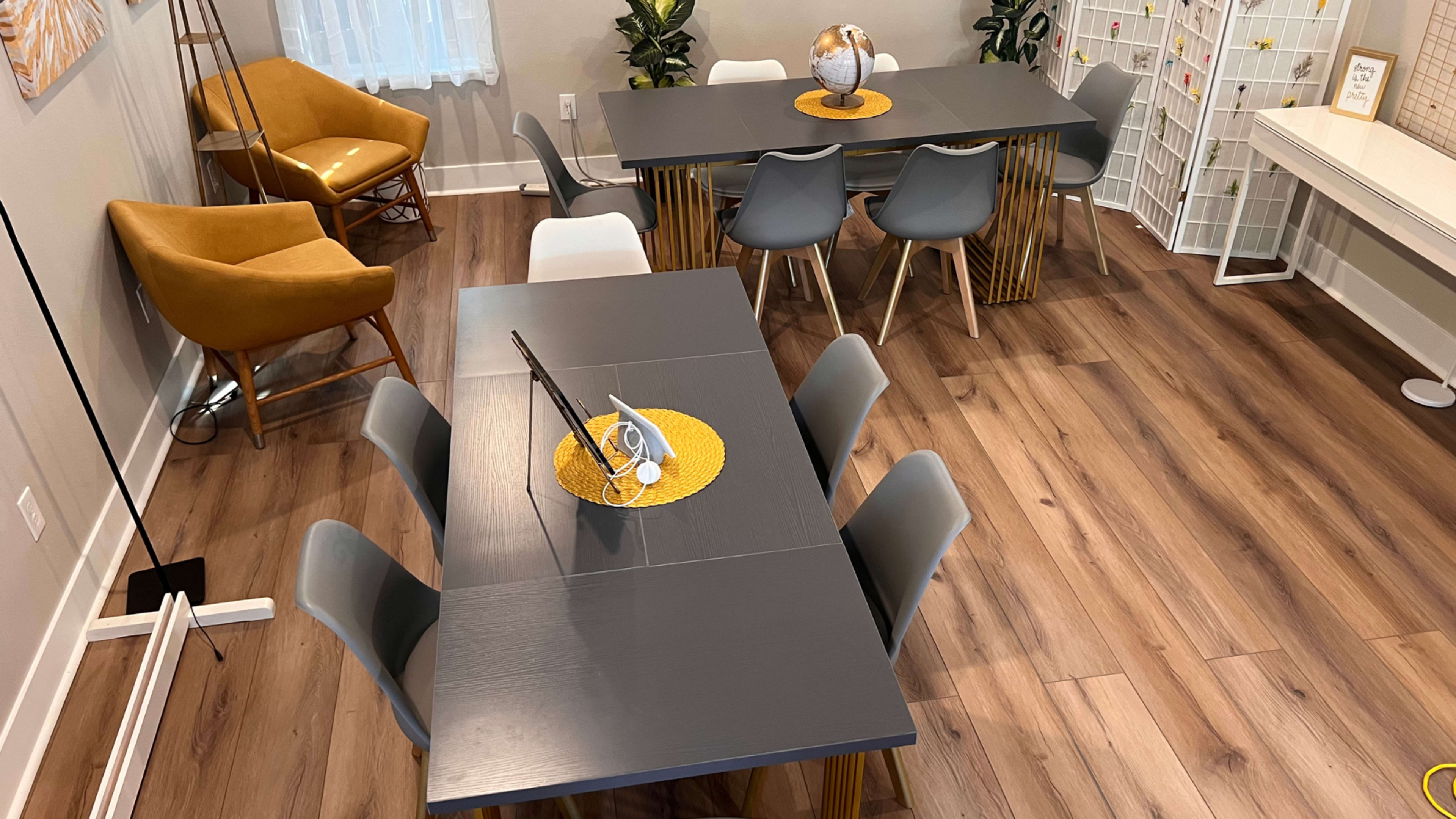 The scene features a modern dining area with two tables, each set with decorative centerpieces, surrounded by chairs and showcasing wooden flooring.