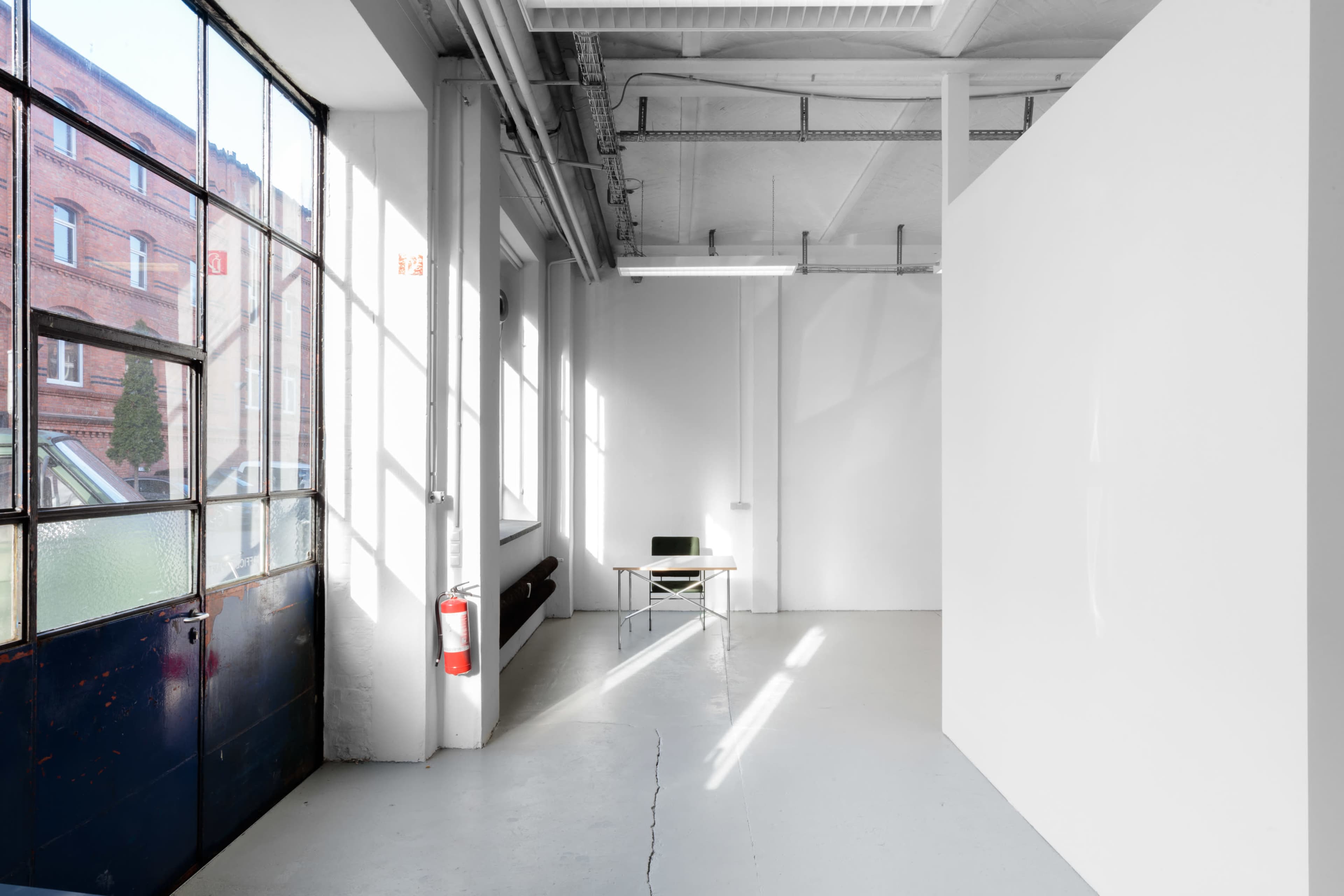 A bright, minimalist room with large windows, a white wall, and a simple table positioned in the corner.