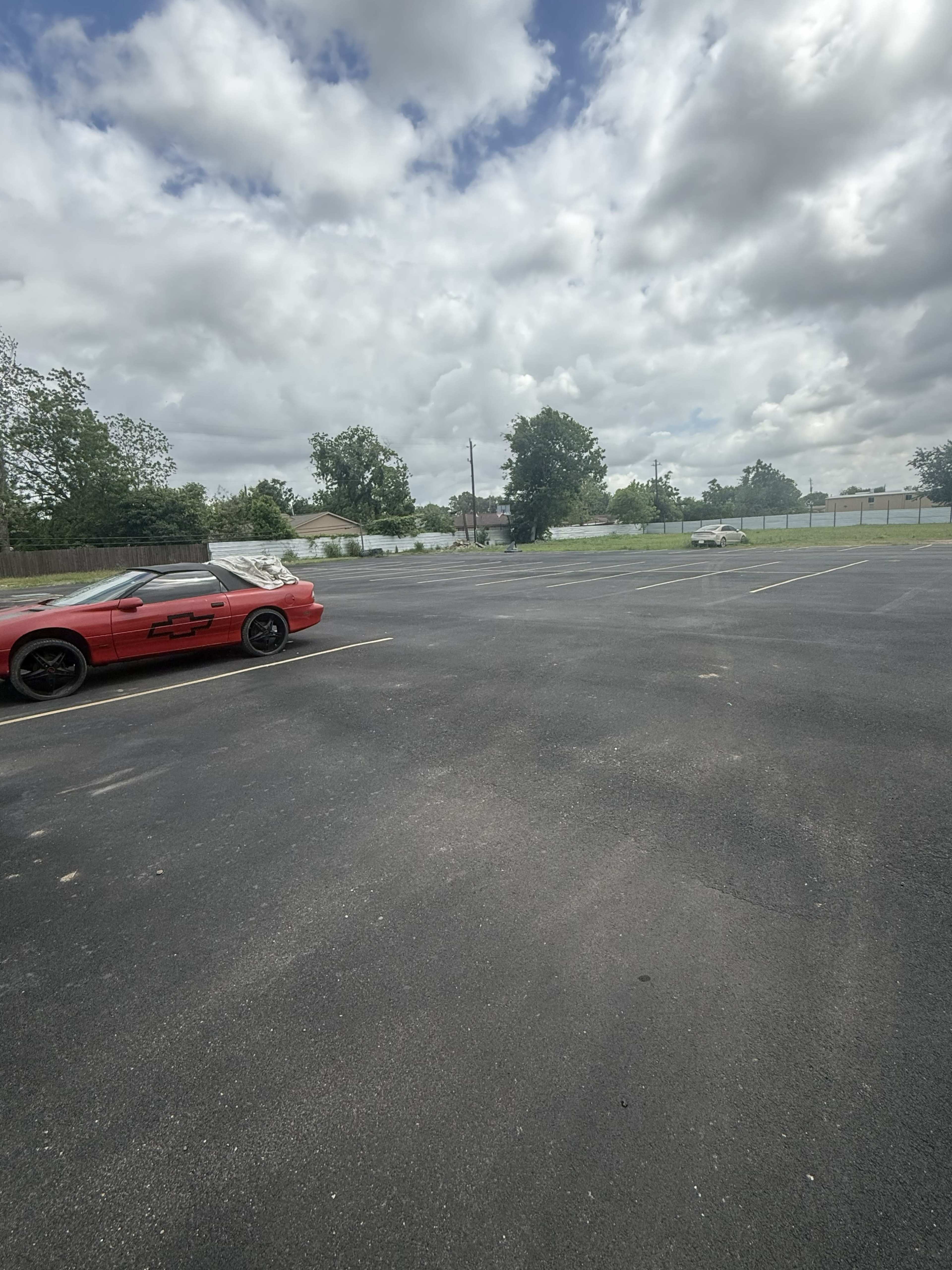 A red sports car is parked in an empty lot under a partly cloudy sky.