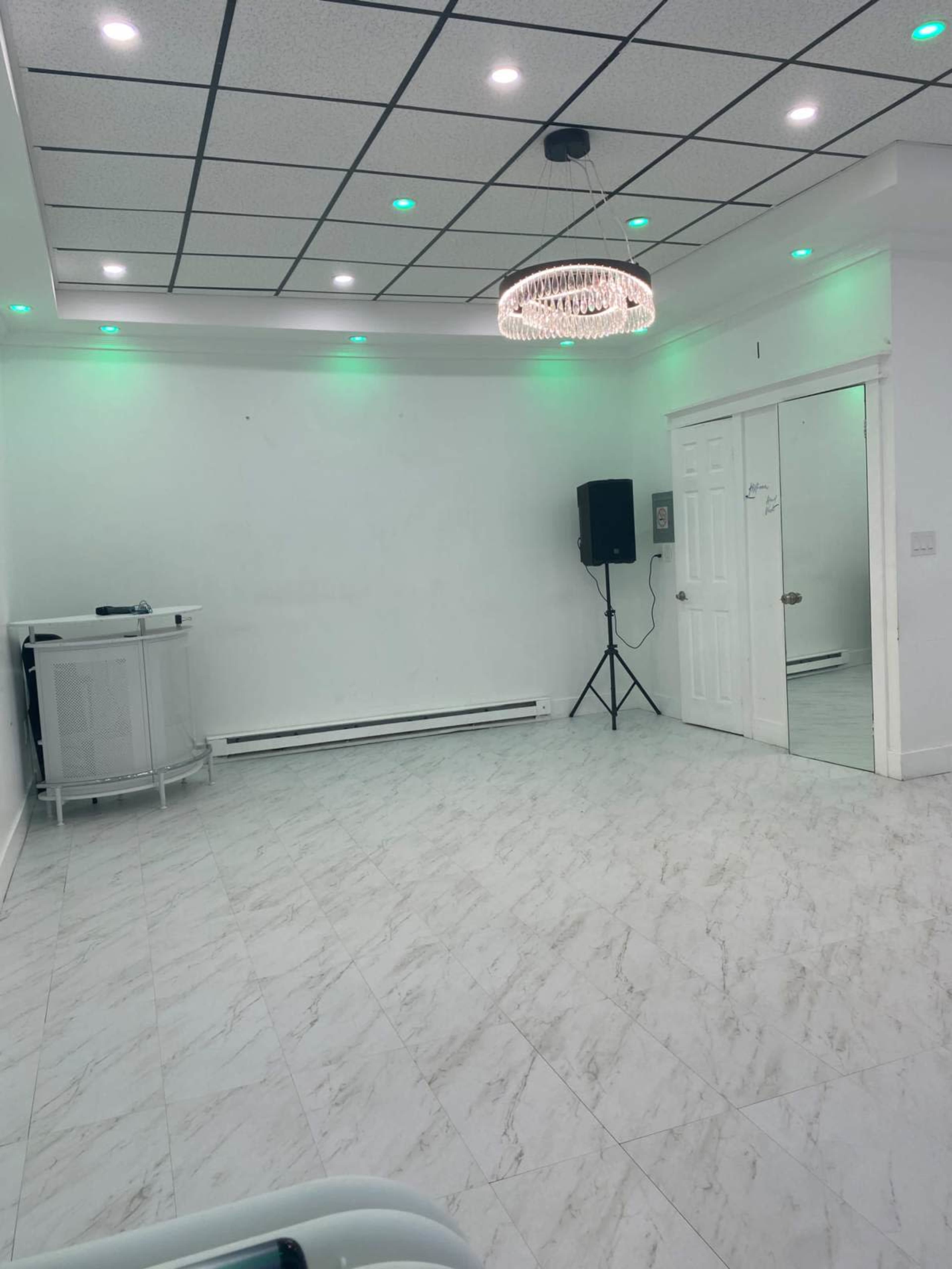 The image shows a spacious room with a marble floor, a decorative chandelier, and green lights illuminating the walls.