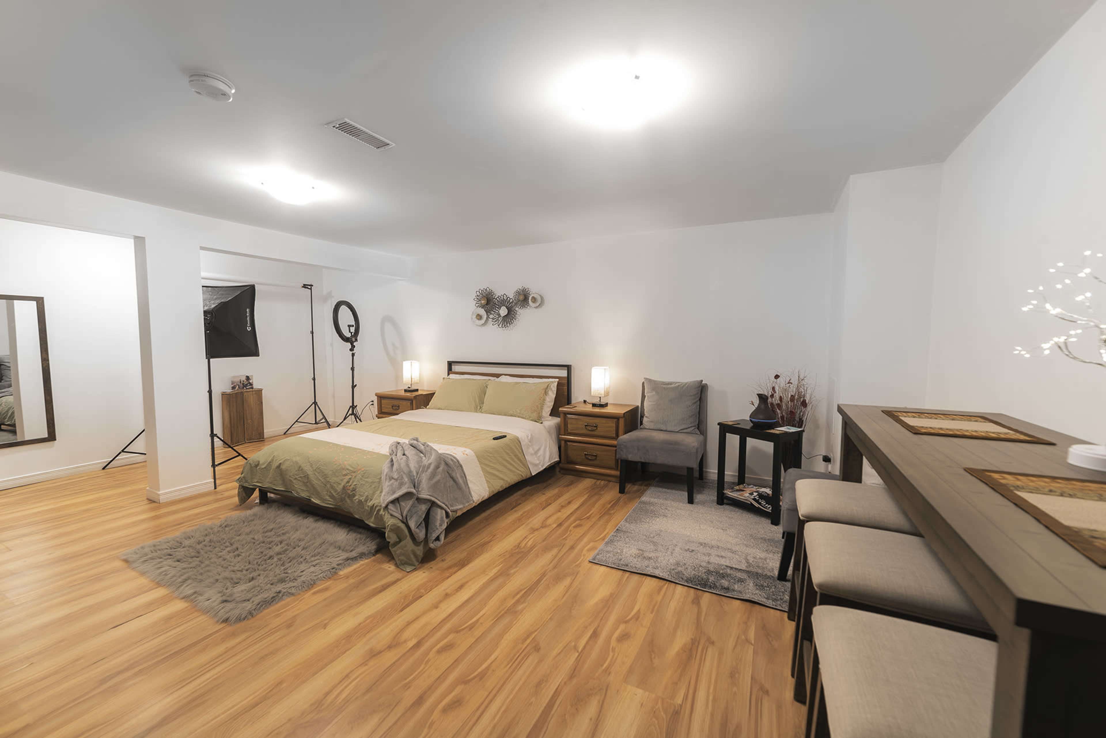 A spacious bedroom with a bed, wooden furniture, and a small seating area, all set on a light wooden floor.
