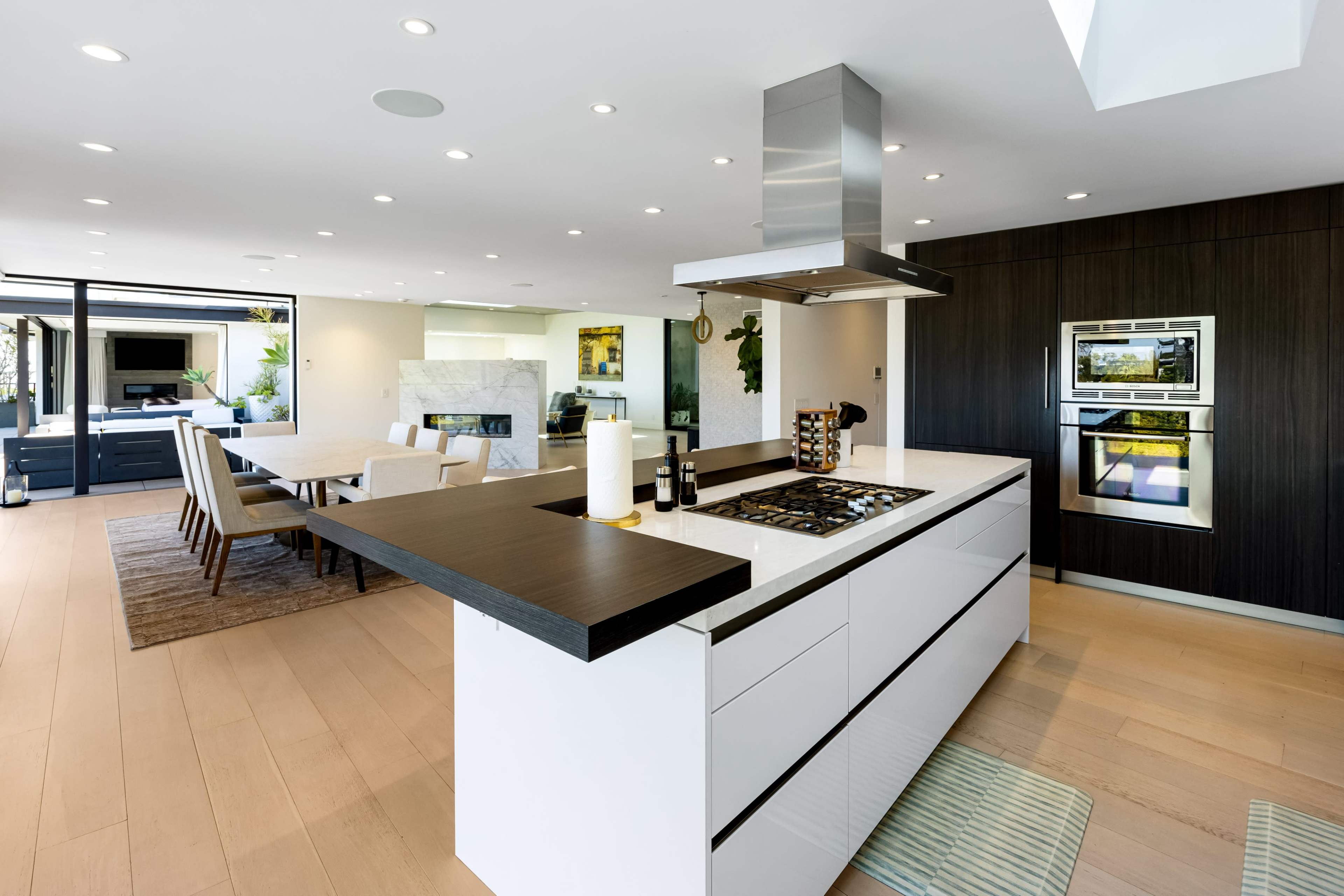 The image shows a modern kitchen with a central island, sleek cabinetry, and an open layout connecting to a dining area.