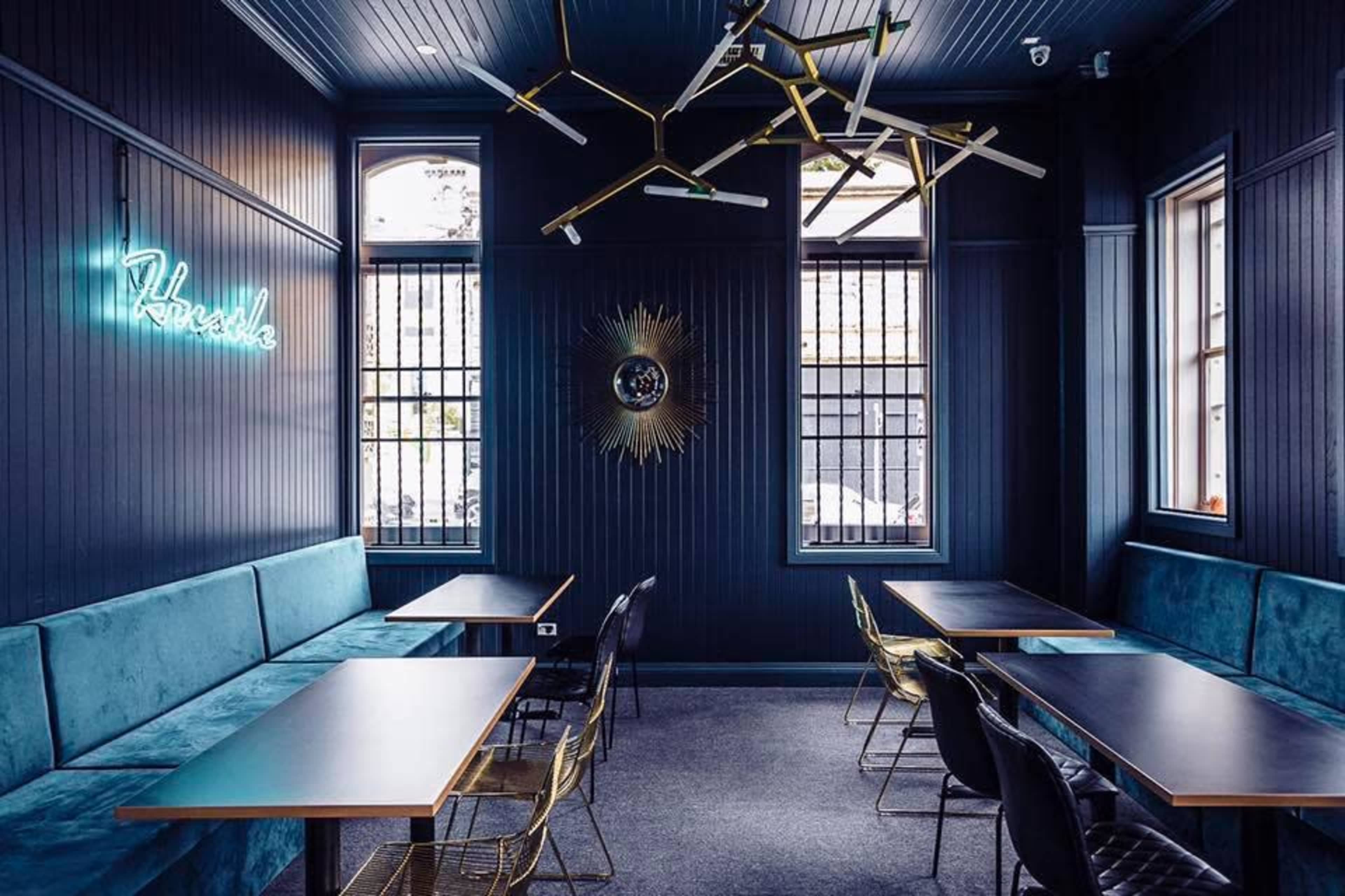 A modern interior of a restaurant with dark walls, gold light fixtures, and teal seating along the windows.