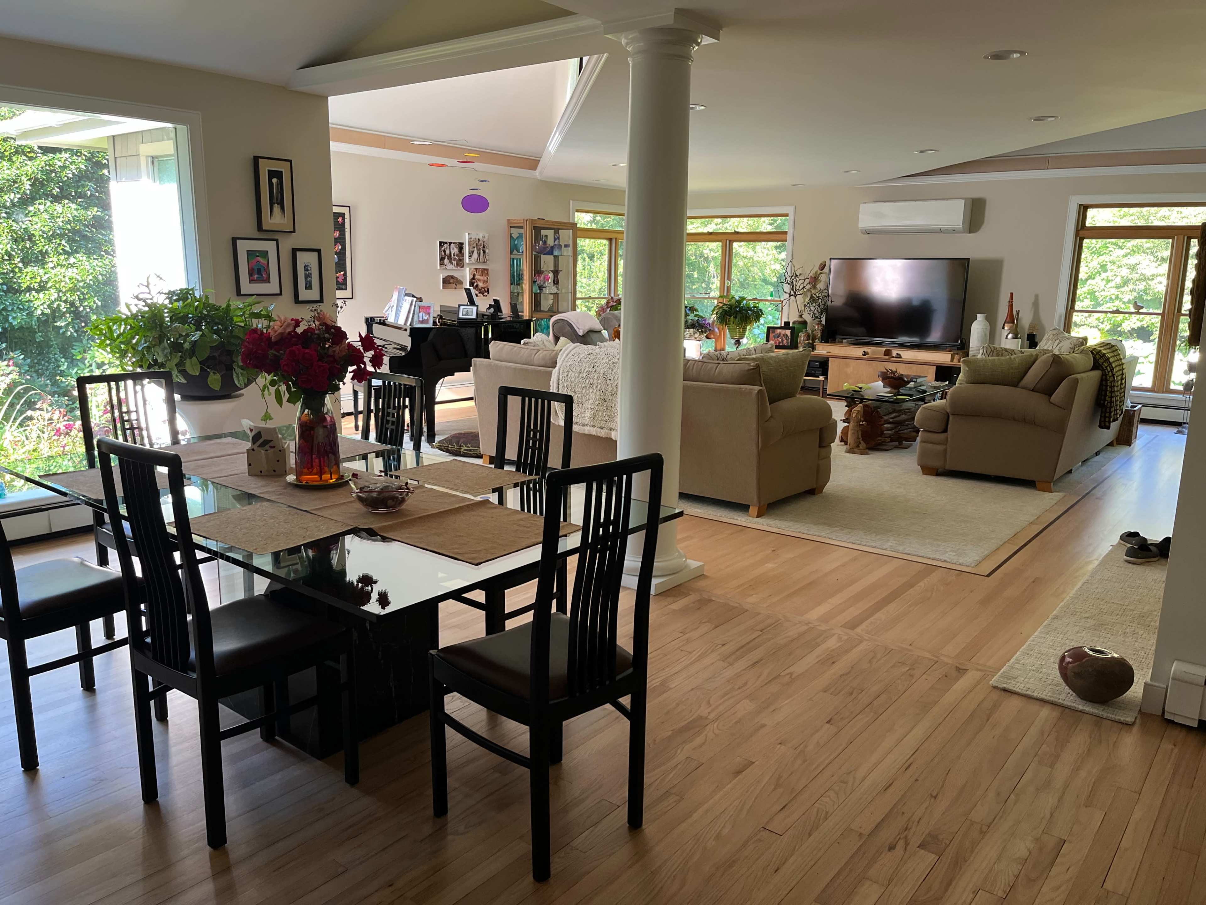 A spacious interior of a home that features a dining area with a glass table and black chairs, leading to a living area with beige sofas and a large television.