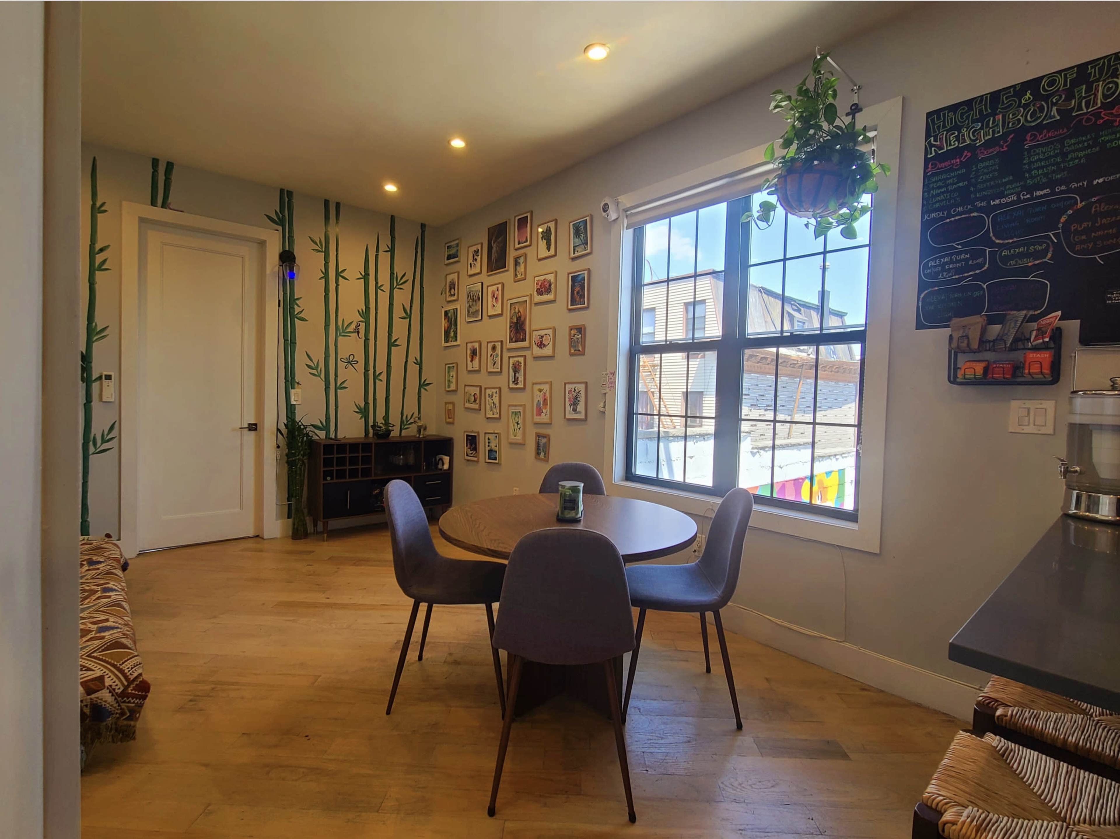 A modern dining area with a round wooden table surrounded by four chairs, bamboo-themed wall decor, and a gallery of framed photos on one wall.