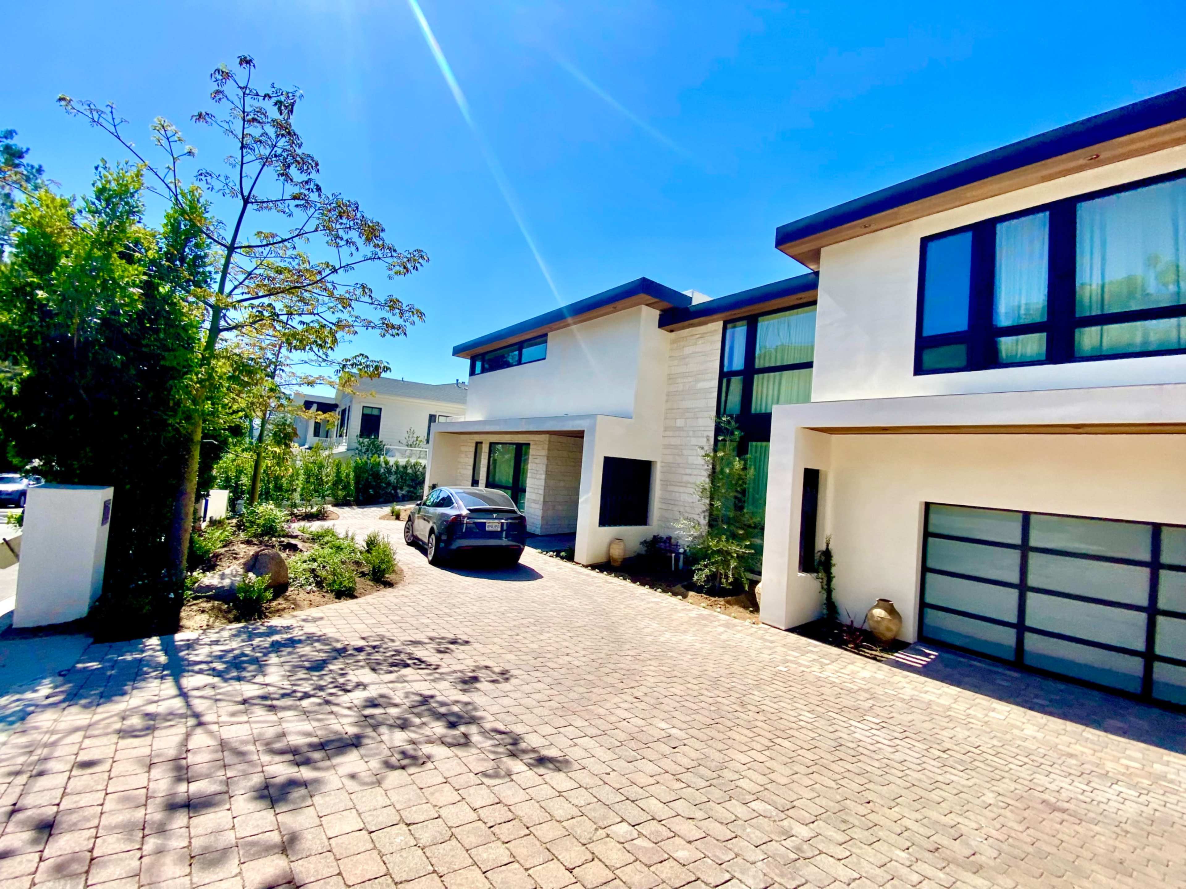 A modern two-story house with large windows sits alongside a paved driveway, leading to a garage.