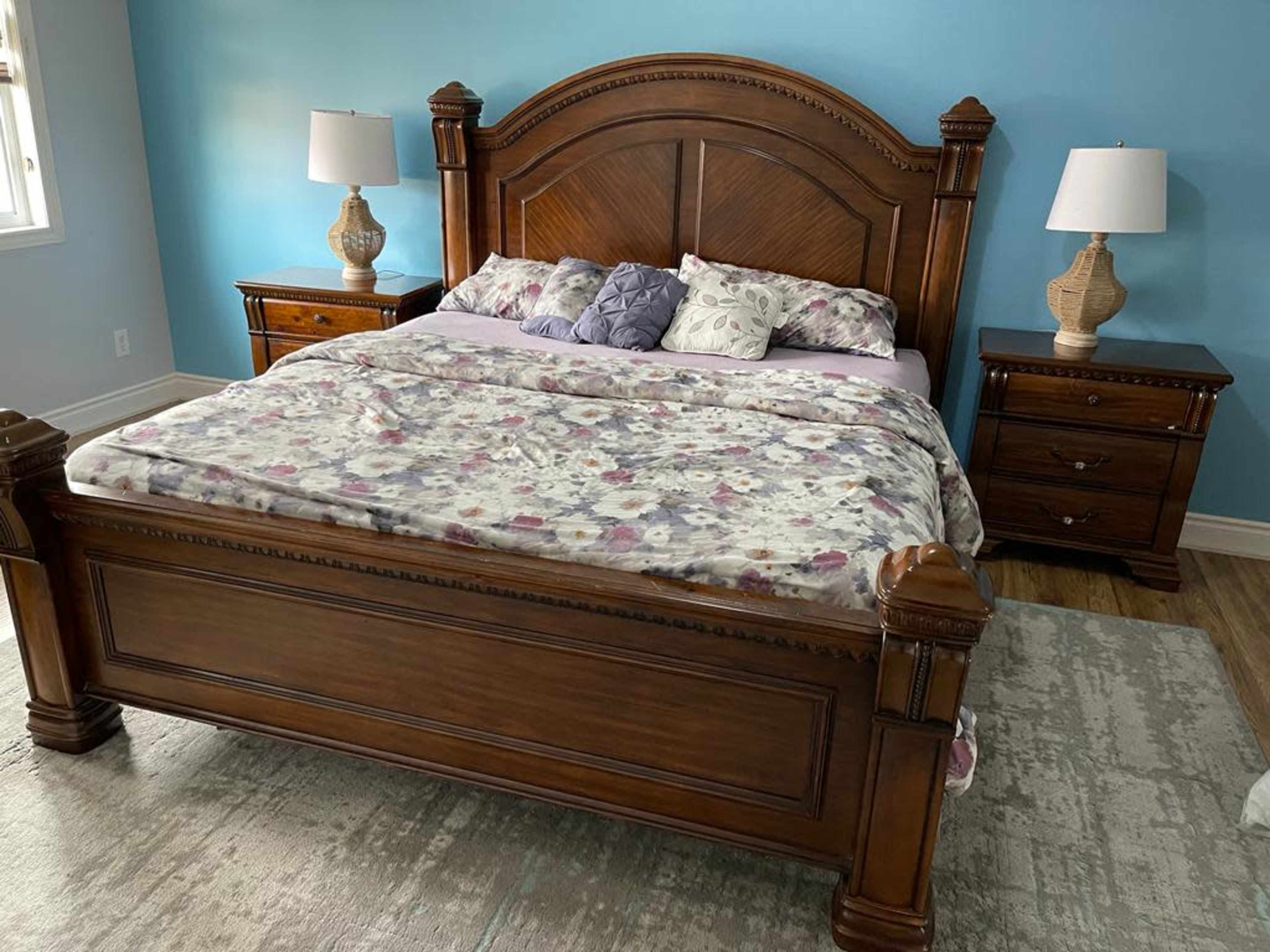 A wooden bed with a floral-patterned blanket, flanked by two bedside tables and lamps, set against a light blue wall.
