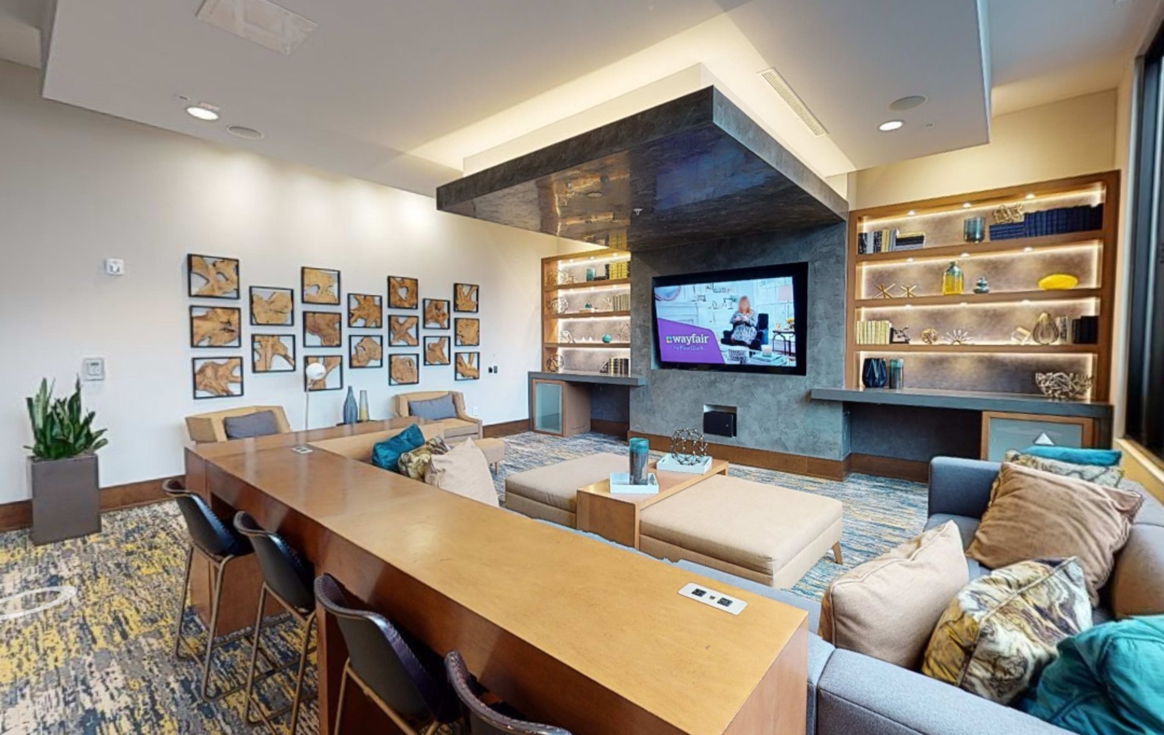 A modern lounge area featuring comfortable seating, a large wall-mounted TV, and decorative shelves illuminated with various items.