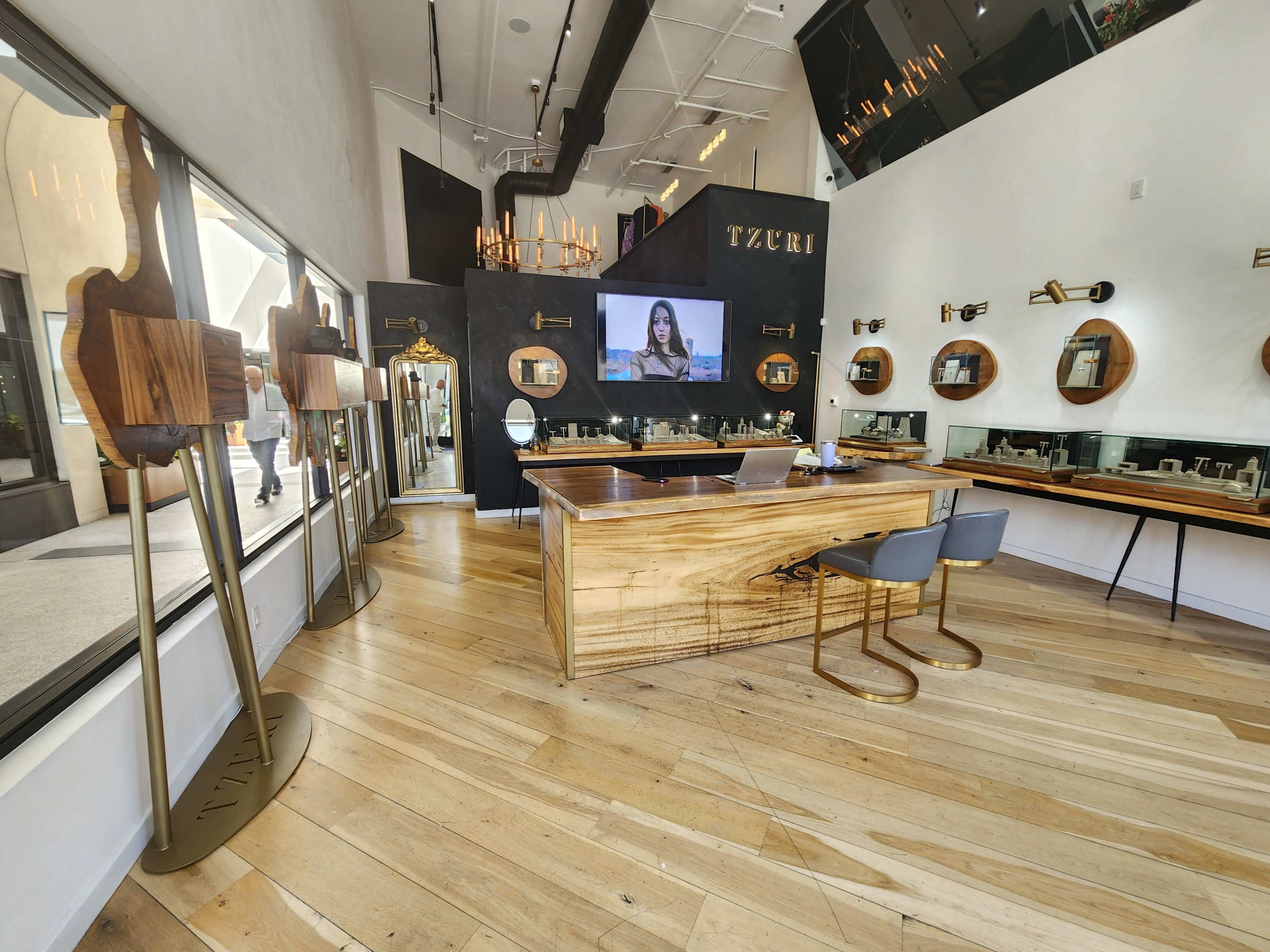 The interior of a modern retail space features a wooden reception desk, mirrors, circular display shelves, and a large screen on the wall.