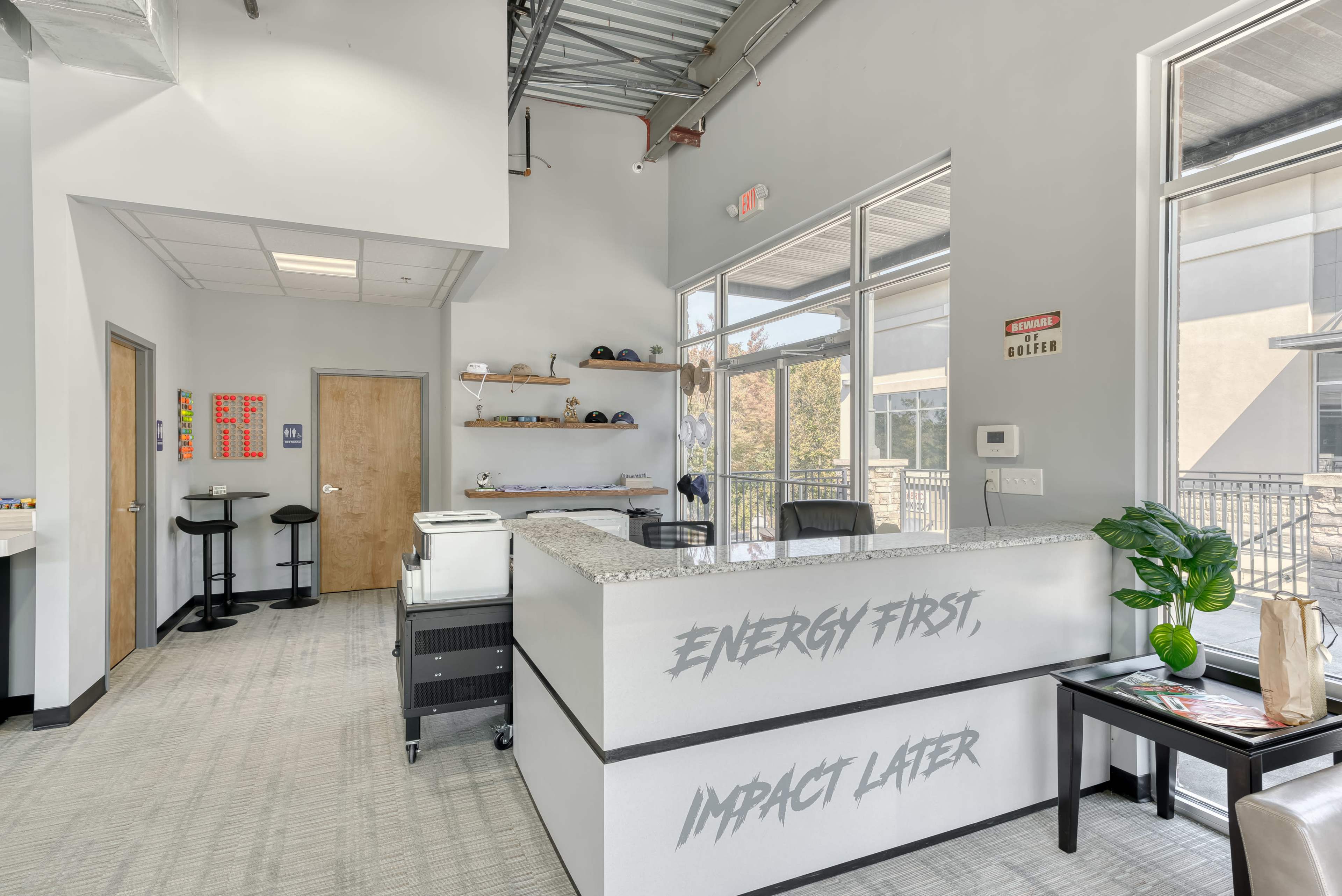 A modern reception area features a gray counter with motivational phrases, surrounding chairs, and shelves displaying various items.