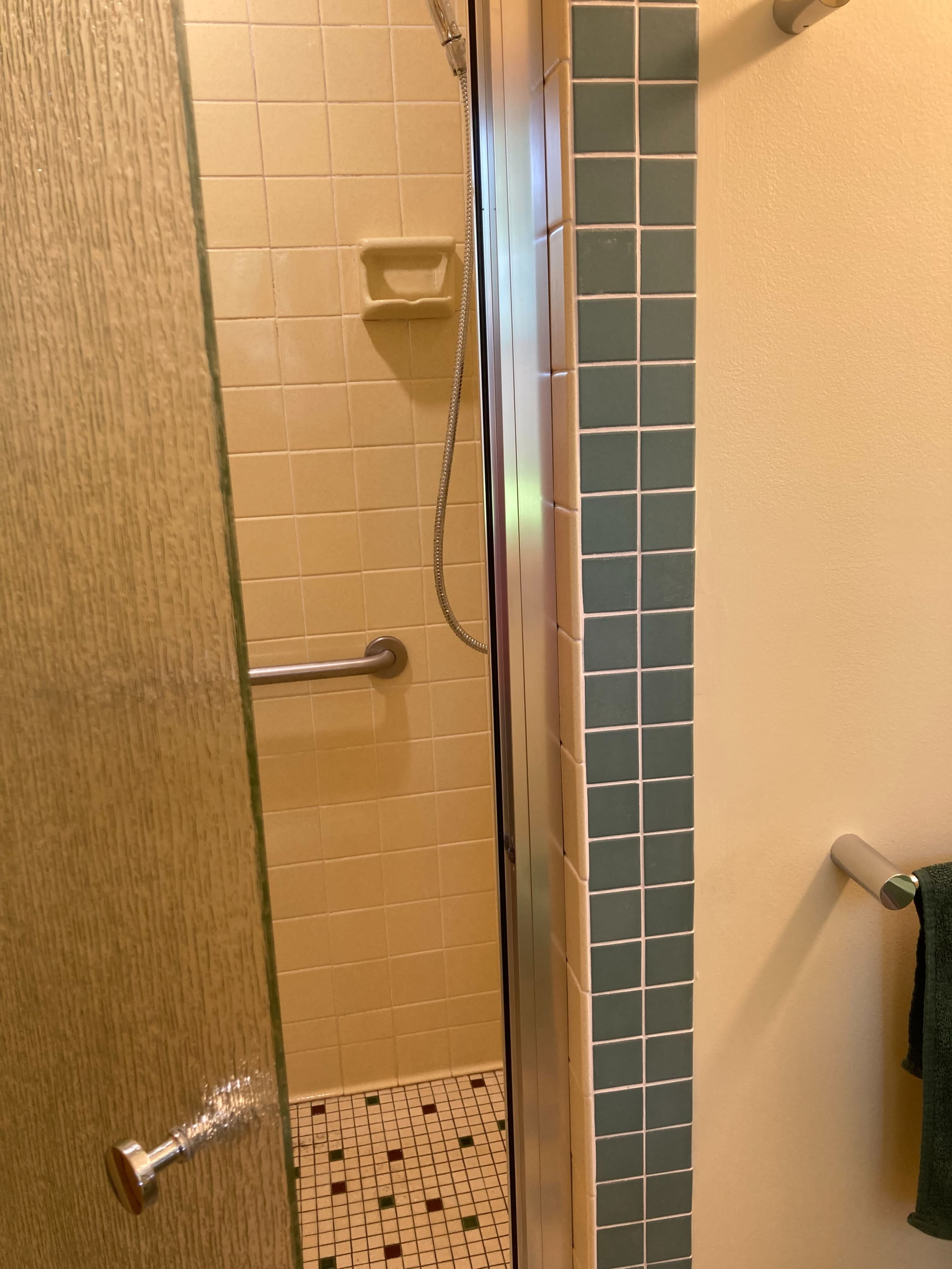 The image shows a small bathroom with a glass shower door, tiled walls, and a showerhead visible inside the shower area.