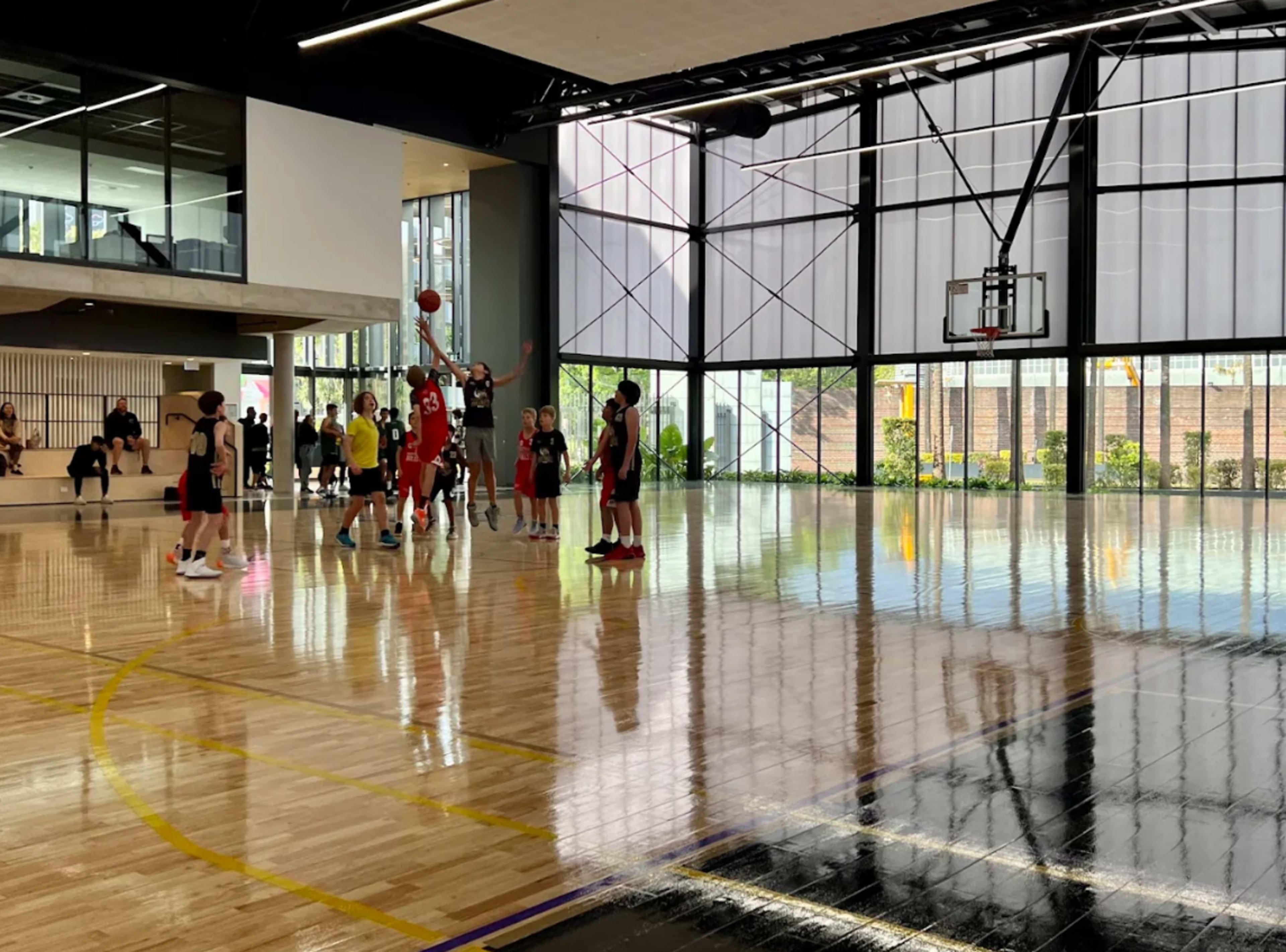 A group of young players is engaged in a basketball game on a polished wooden court, with one player shooting a basketball towards the hoop.