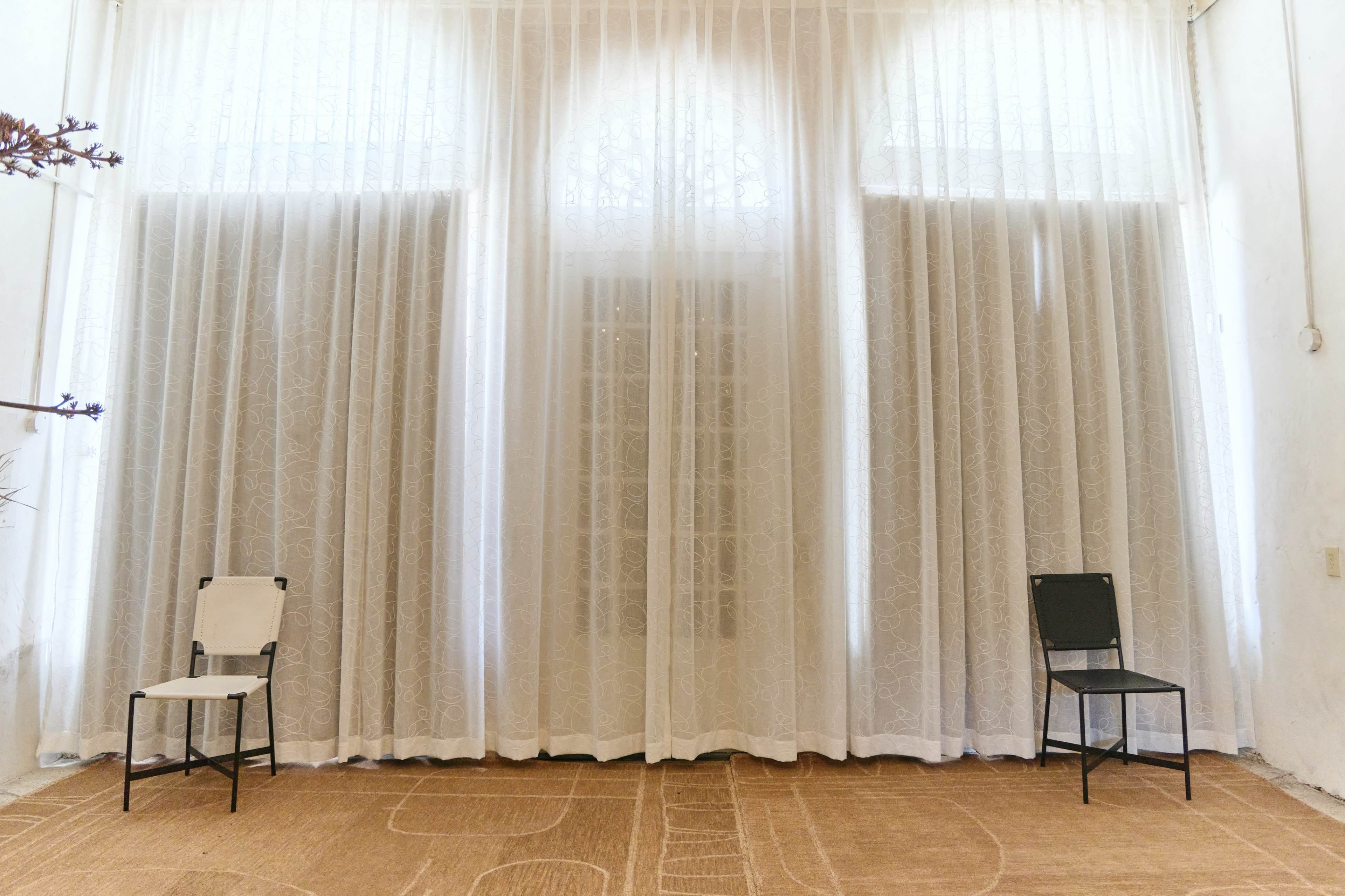 The image shows a spacious room with two chairs placed near a large curtain that covers a window.