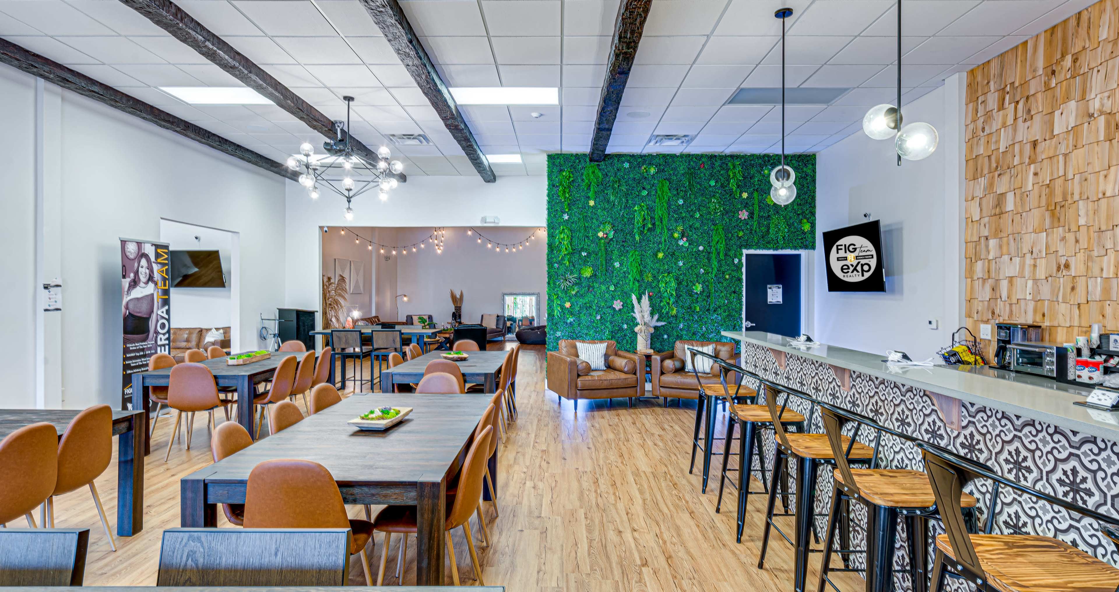 A modern, open-layout event space featuring wooden flooring, a green accent wall, and various seating options including tables and a lounge area.