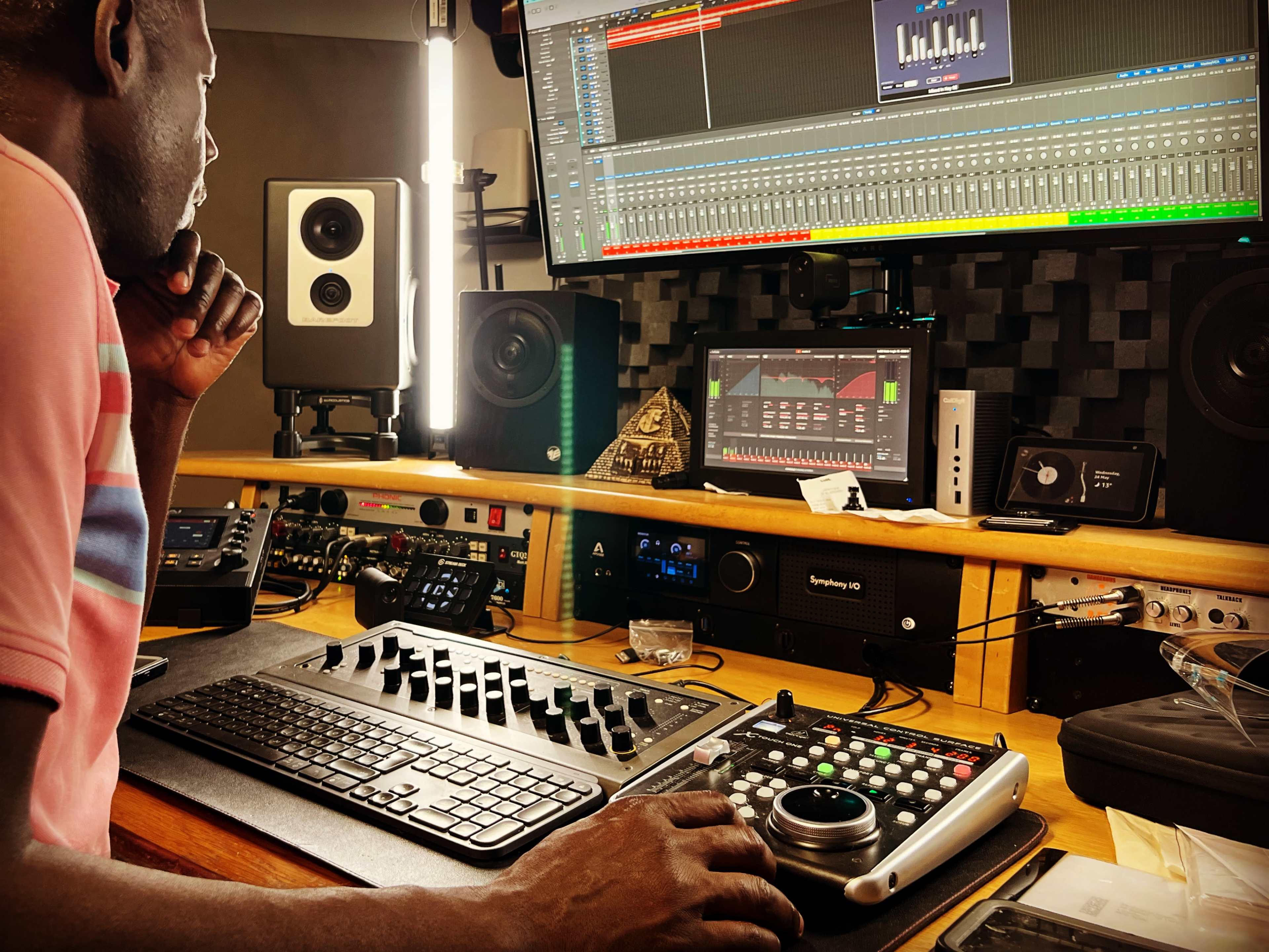 A person is working at a music production desk surrounded by audio equipment and multiple monitors displaying sound editing software.