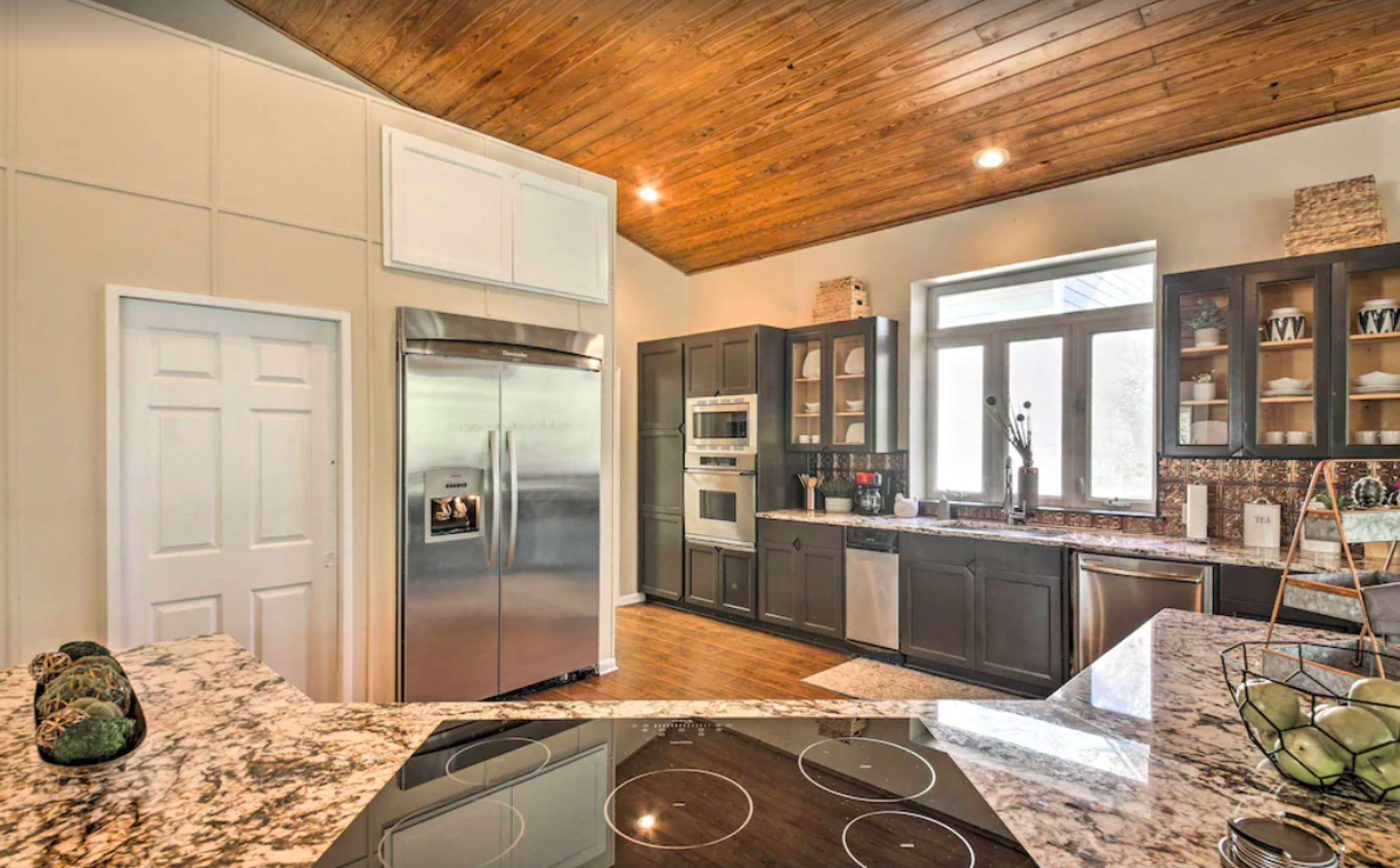 A modern kitchen featuring stainless steel appliances, dark cabinetry, and a granite countertop with a wooden ceiling.