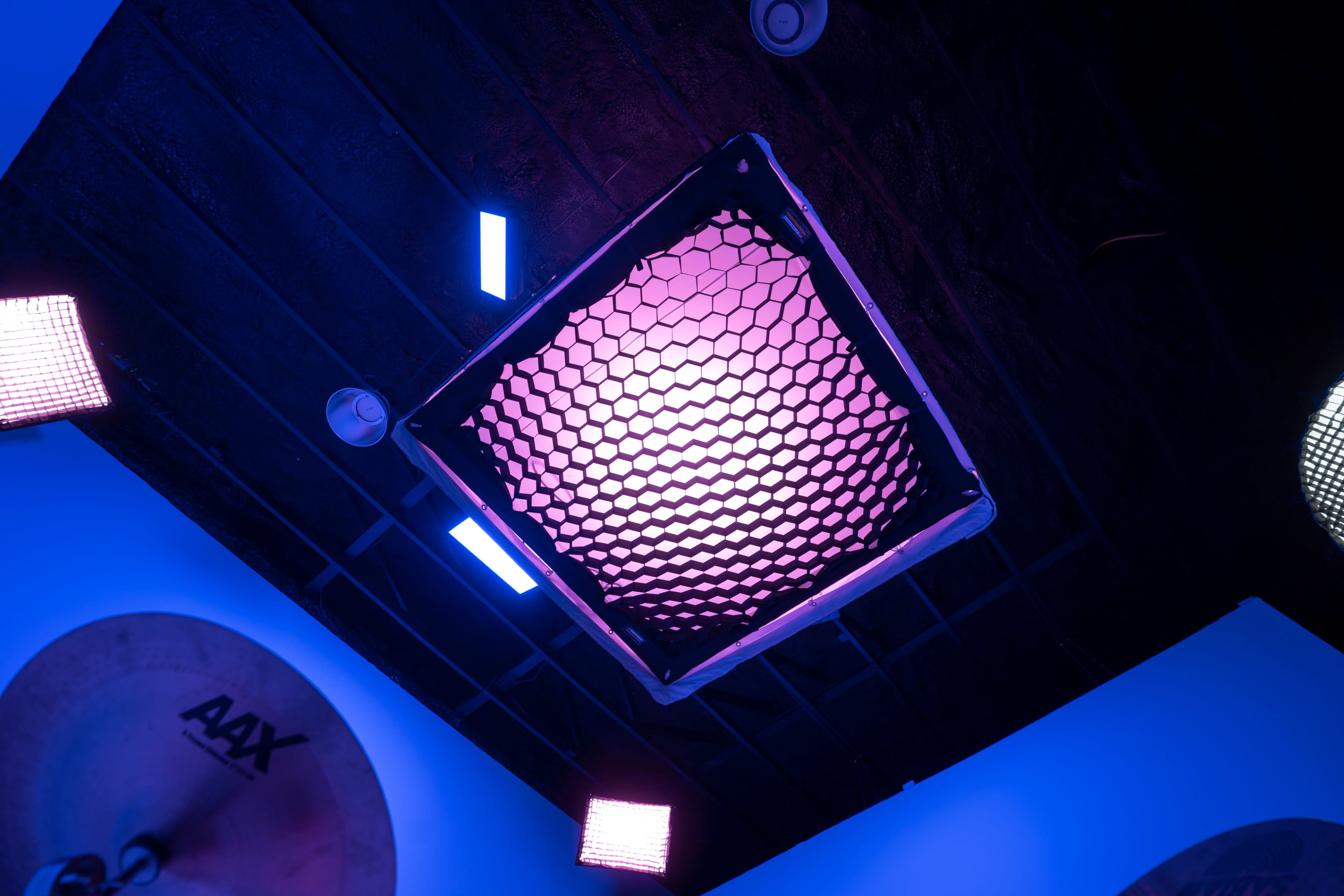 A ceiling light with a hexagonal grid pattern emits purple and blue light in a dimly lit room.