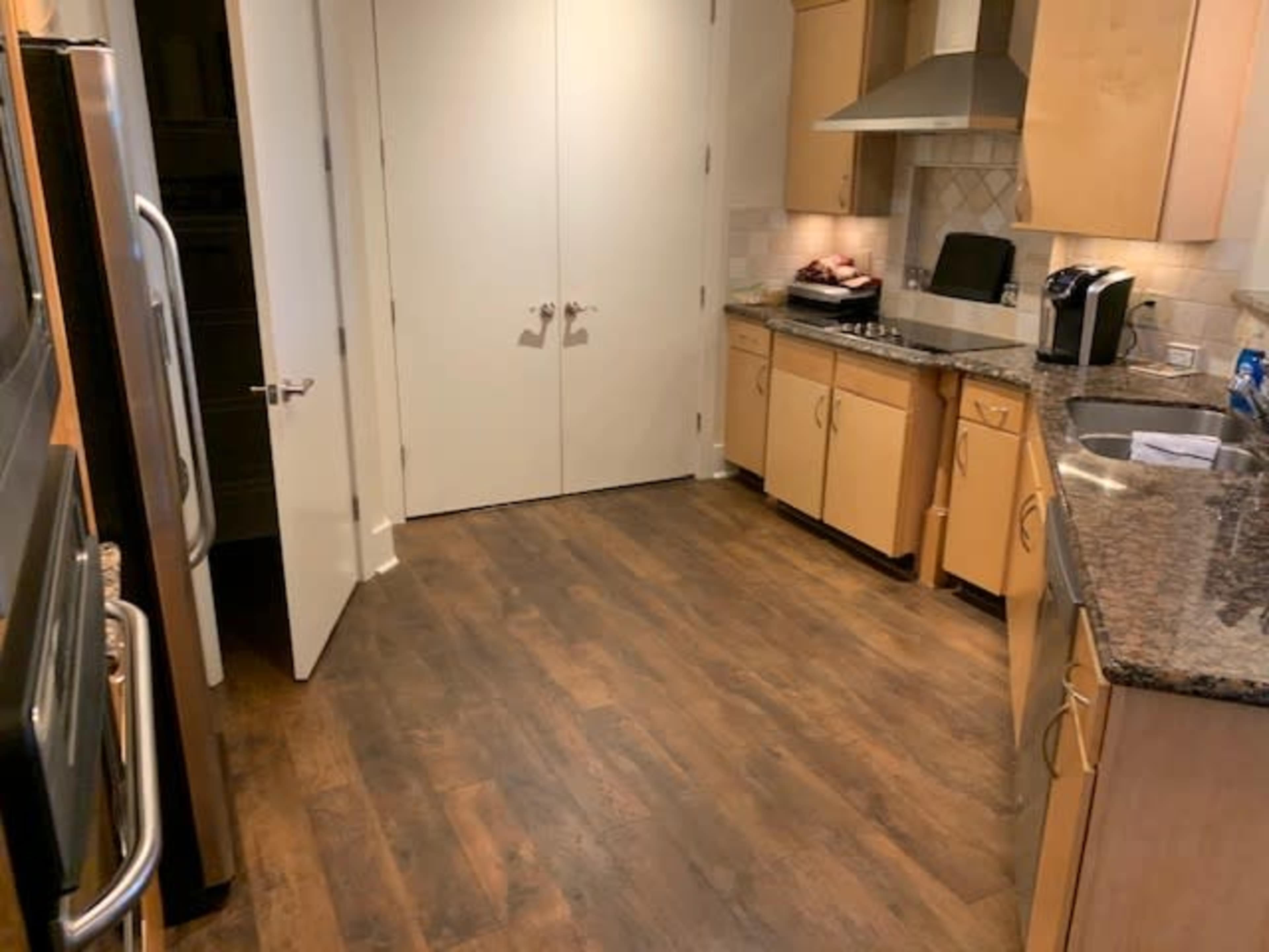 A kitchen features wooden floors, wooden cabinetry, stainless steel appliances, and a countertop with a stove and sink.