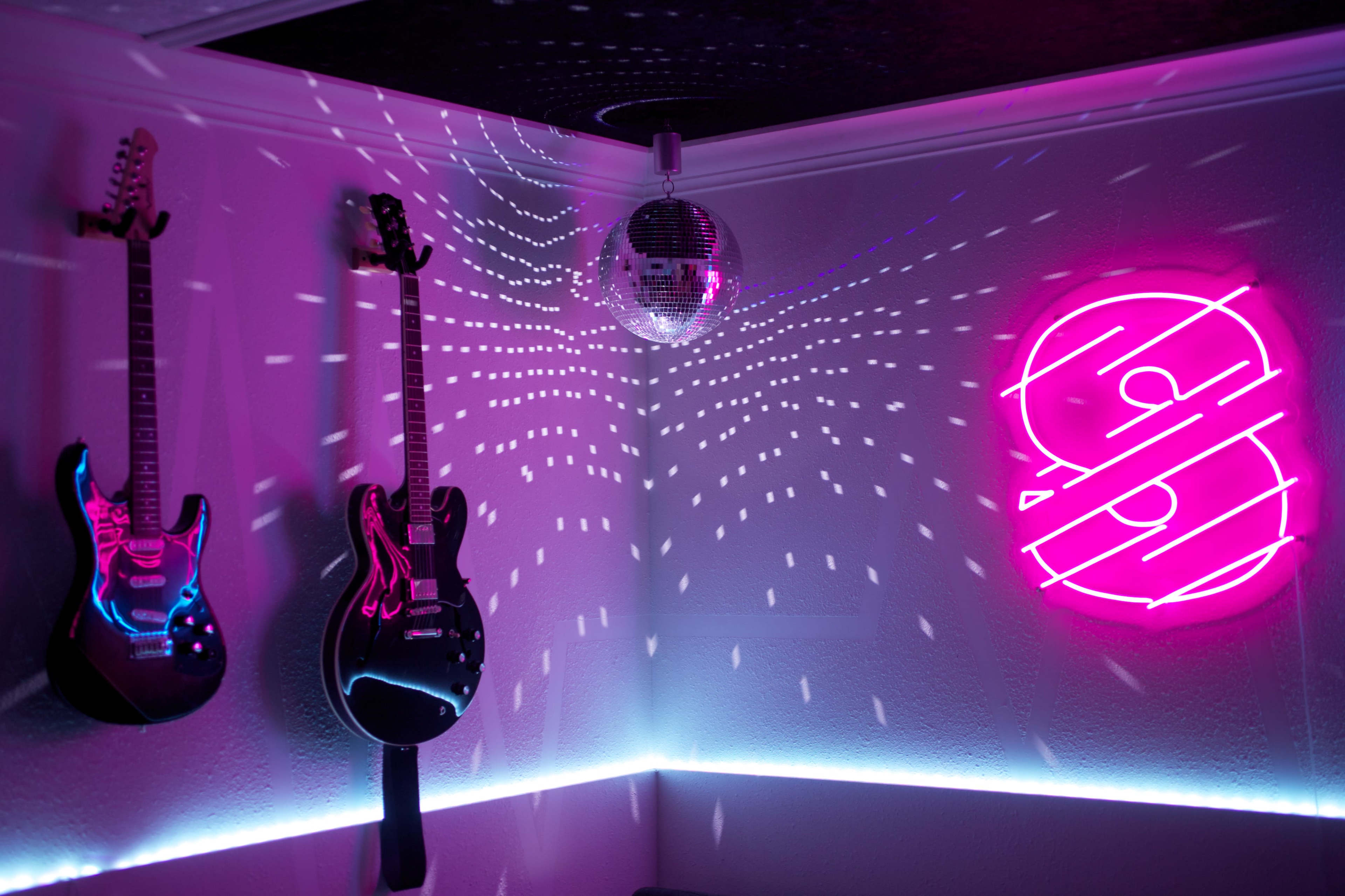 The image features two electric guitars hanging on a wall with a disco ball above and vibrant colored lights creating patterns on the ceiling.