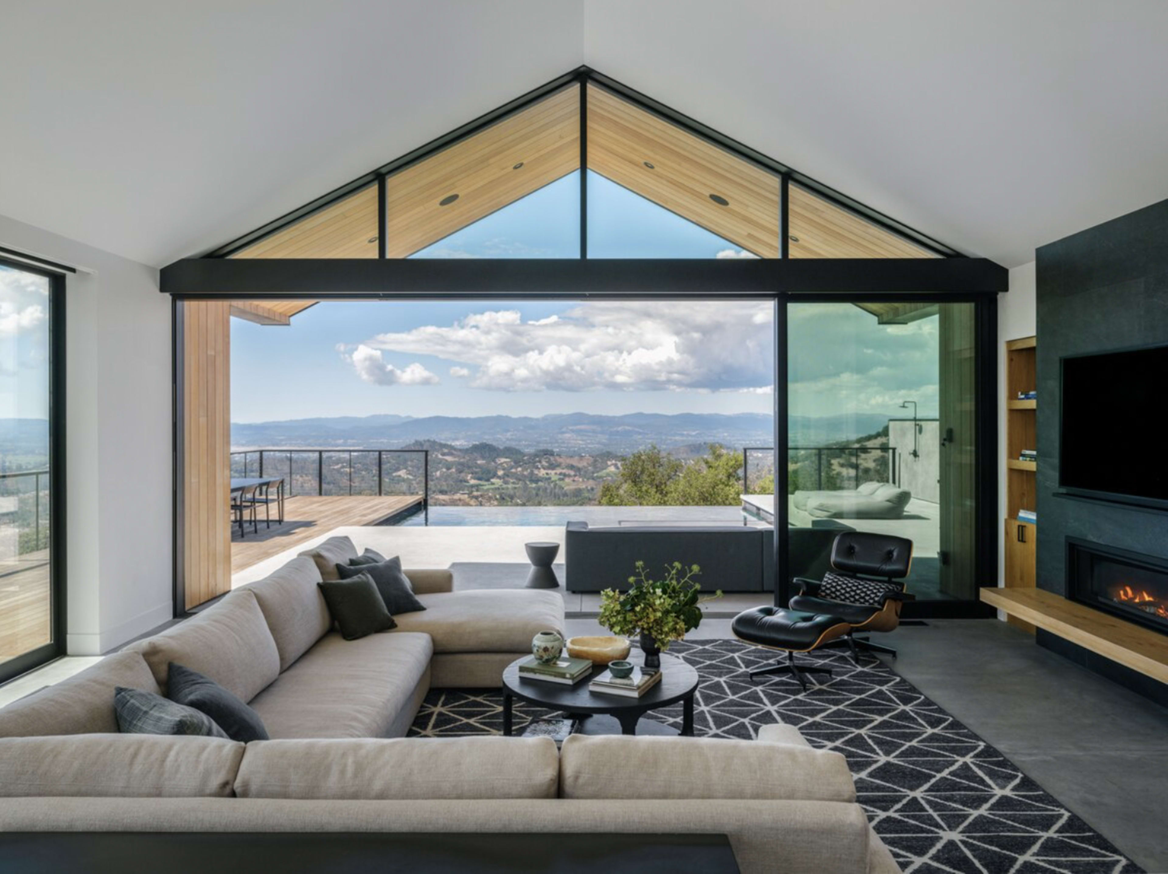 A modern living room with a large sectional sofa, a coffee table, and expansive windows offering a view of a mountainous landscape.