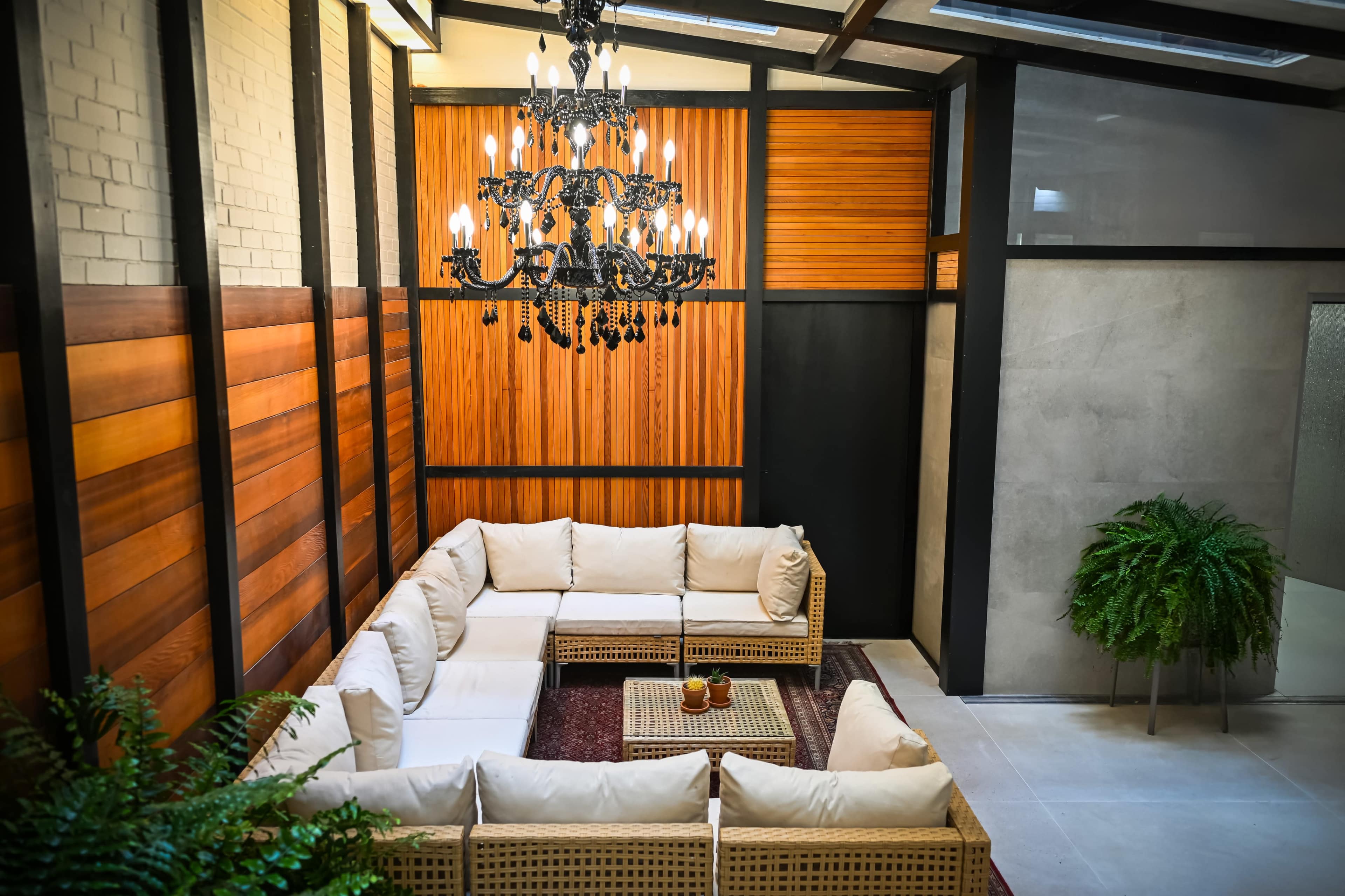 A modern living space features a large white sectional sofa arranged around a coffee table, with a chandelier overhead and plants in the corner.