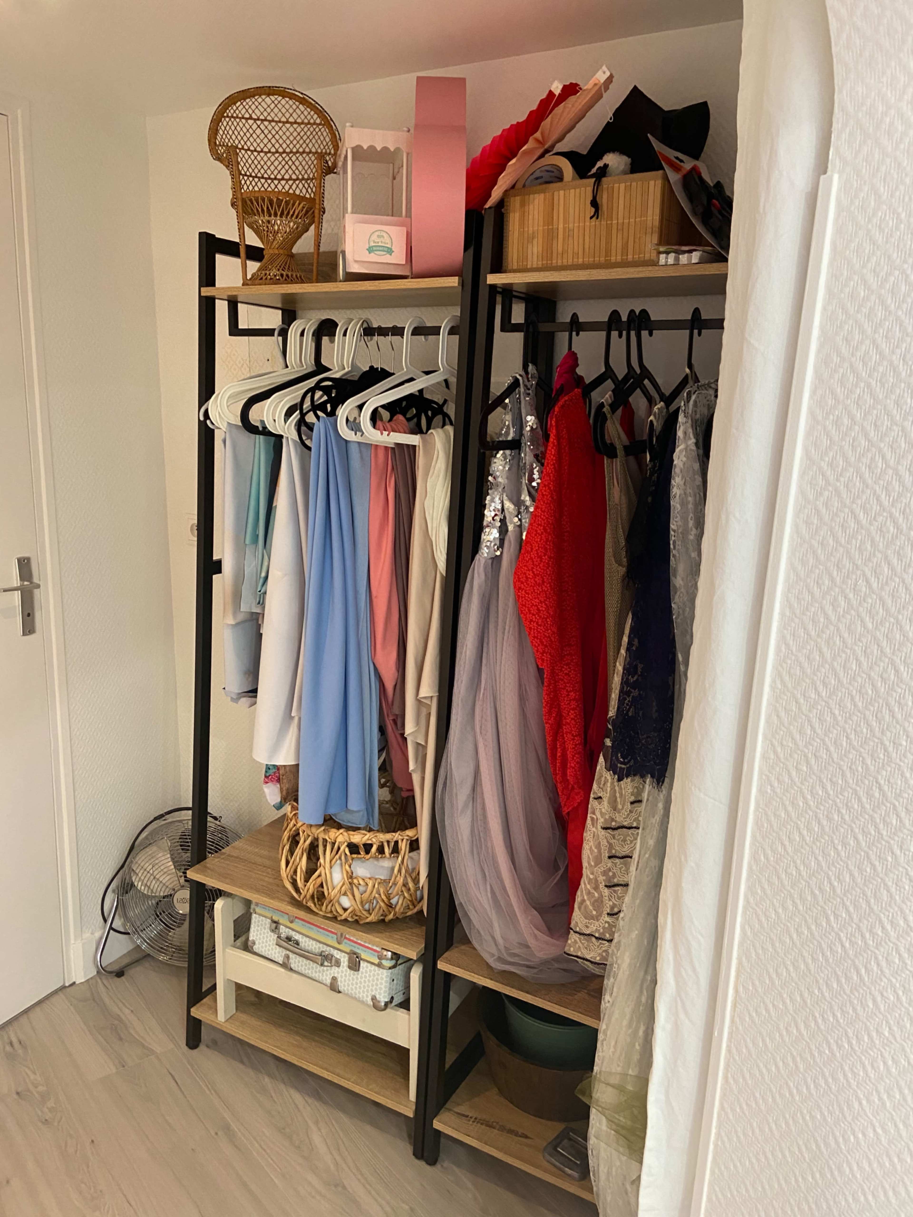 A clothing rack with various garments hanging, along with storage baskets and boxes placed on shelves.