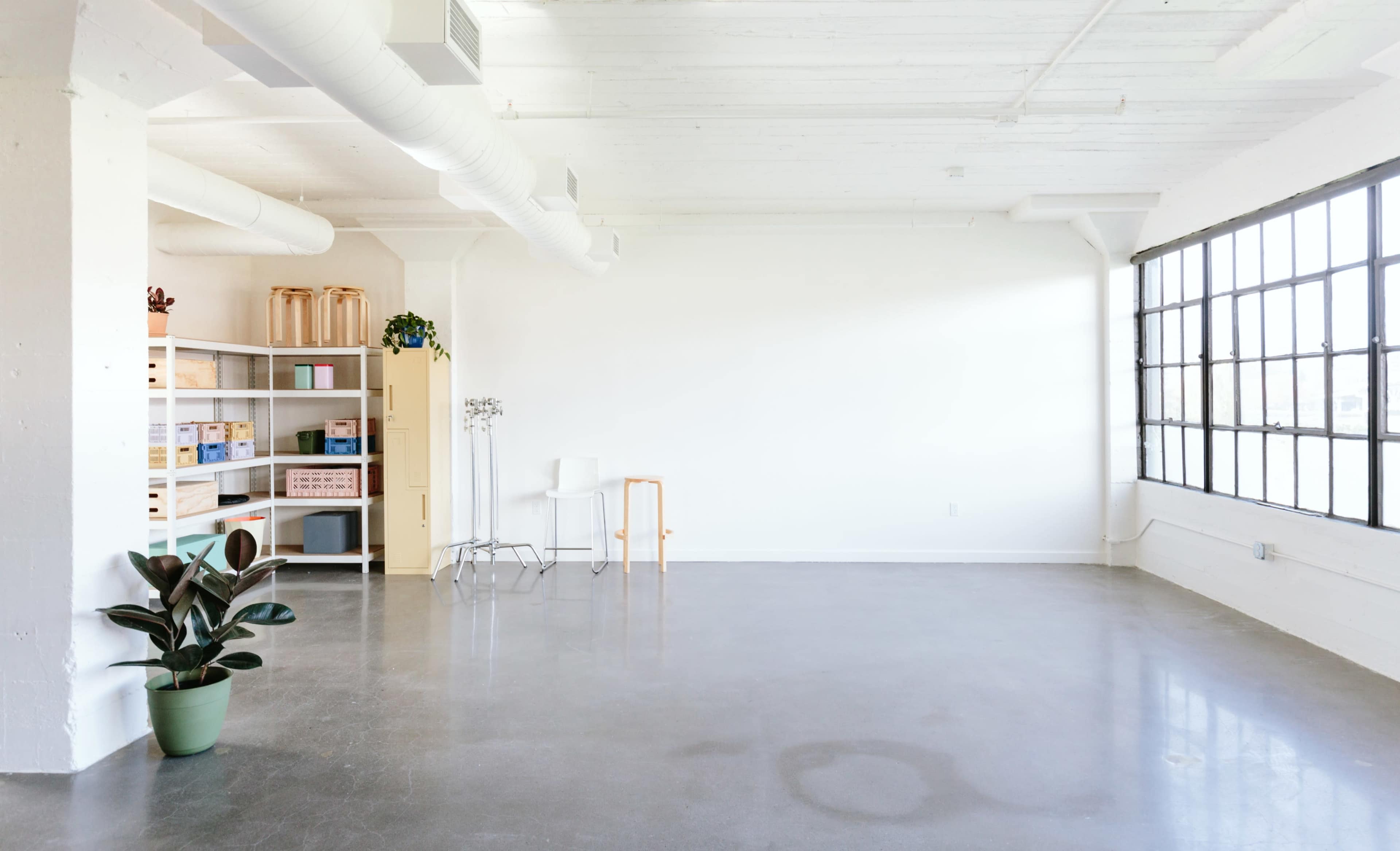 An empty, well-lit interior space with polished concrete flooring, a large window, and a shelf containing organized storage boxes.