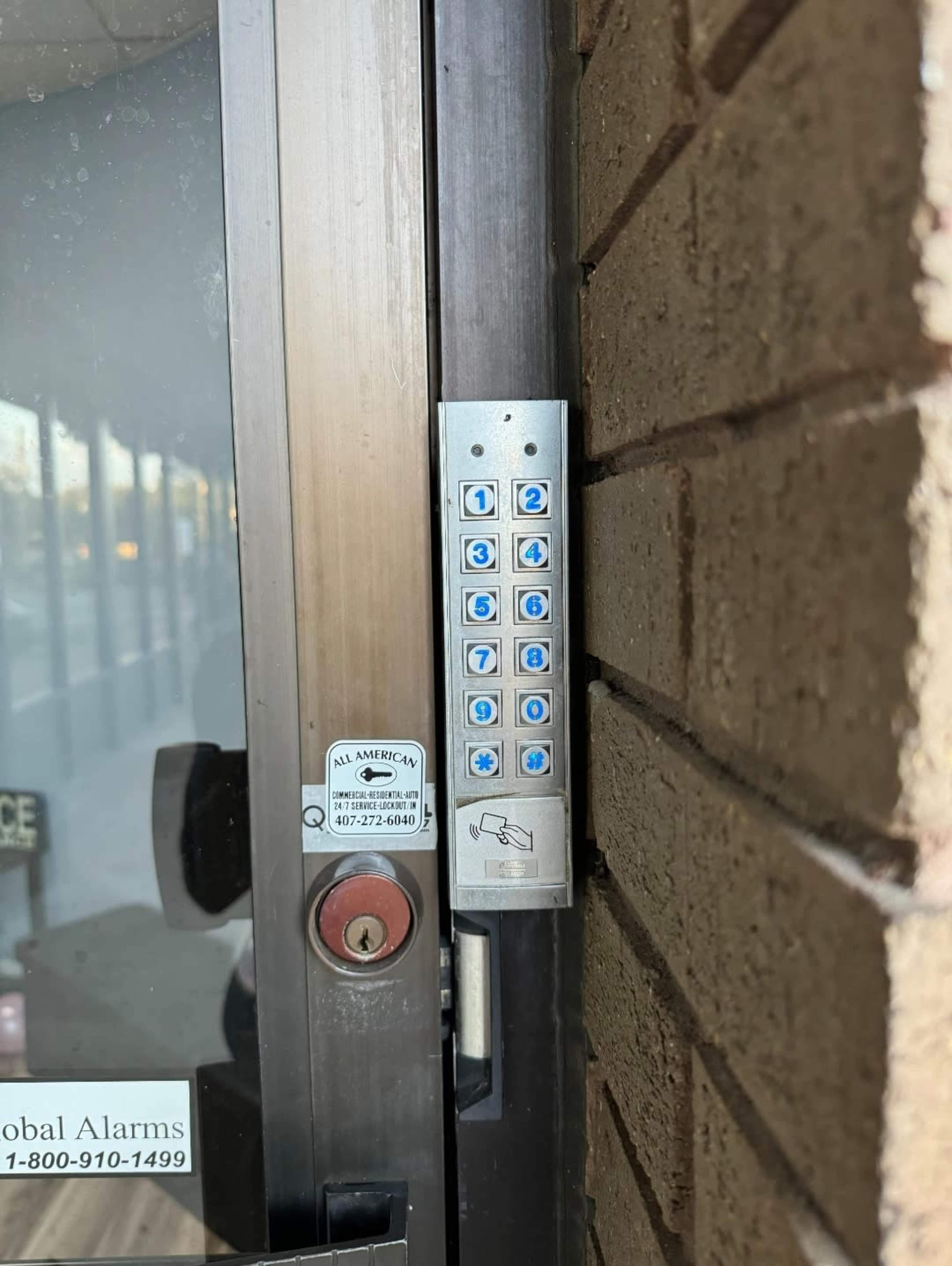 A keypad mounted on a doorframe, featuring numeric buttons and a card reader, alongside an alarm system sticker.