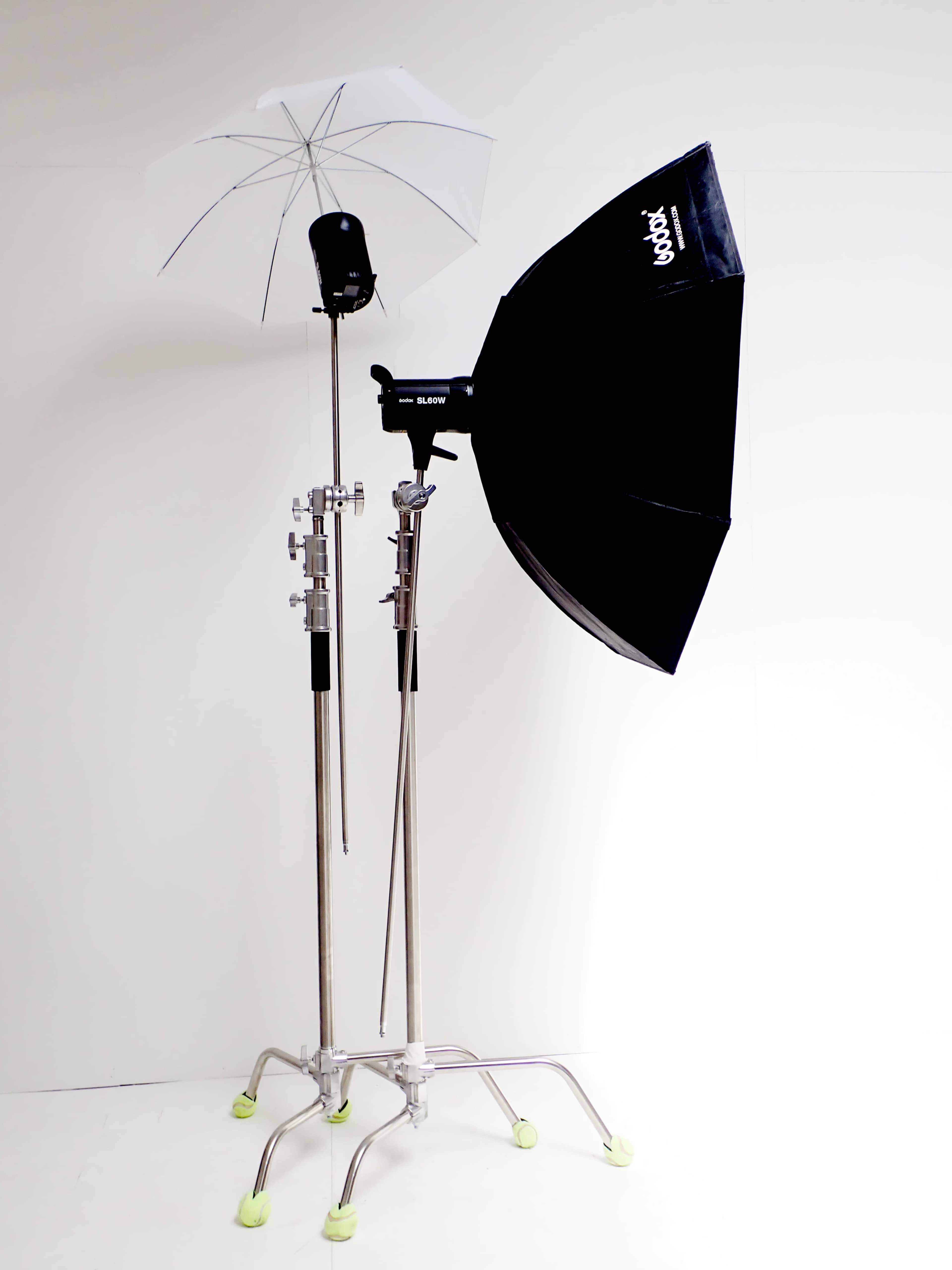 The image shows two studio lighting setups, one with an umbrella and the other with a softbox, both mounted on adjustable stands.