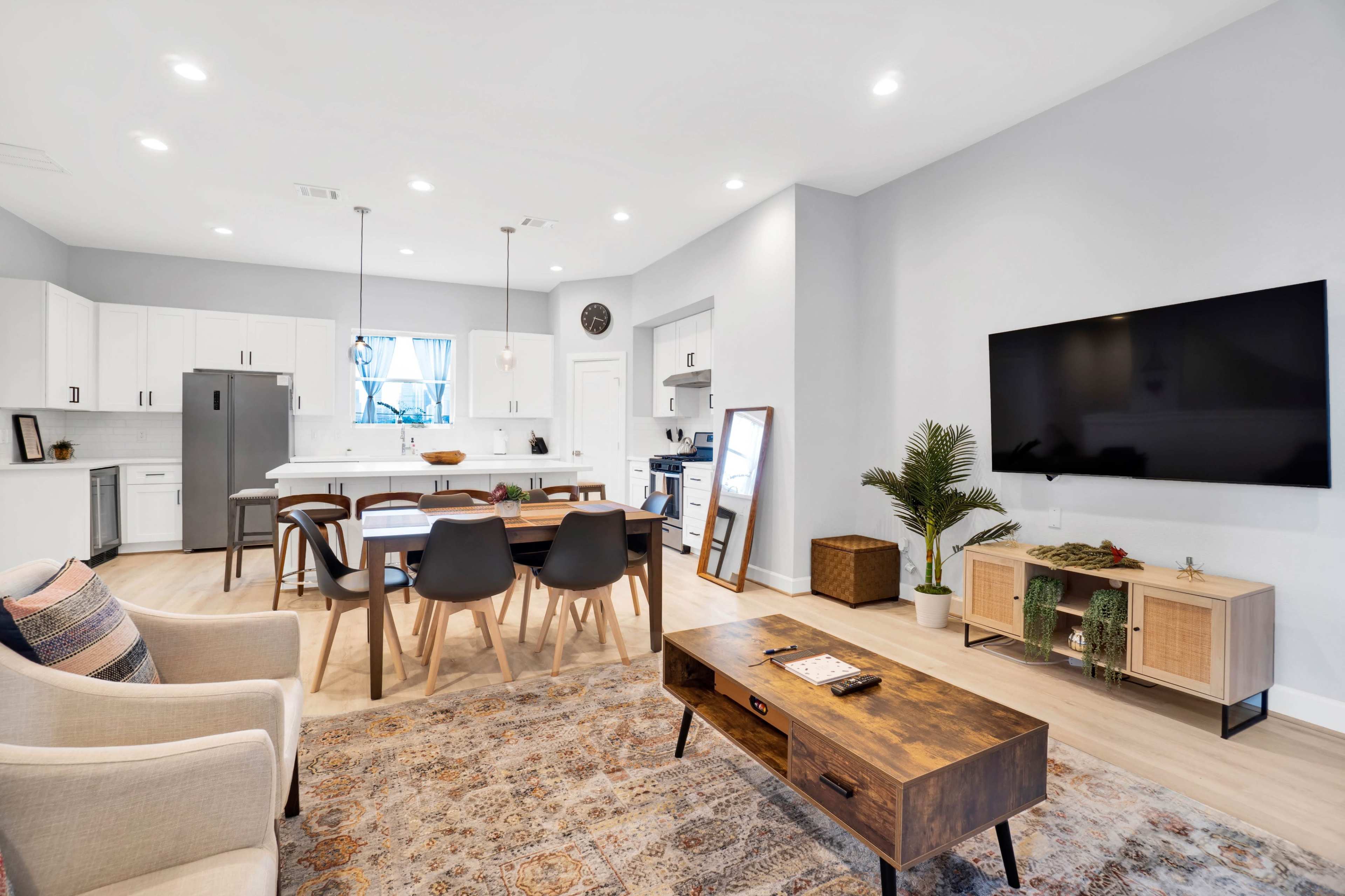 A modern living and dining area with a sectional sofa, a wooden coffee table, and a kitchen in the background featuring white cabinets and a large island.