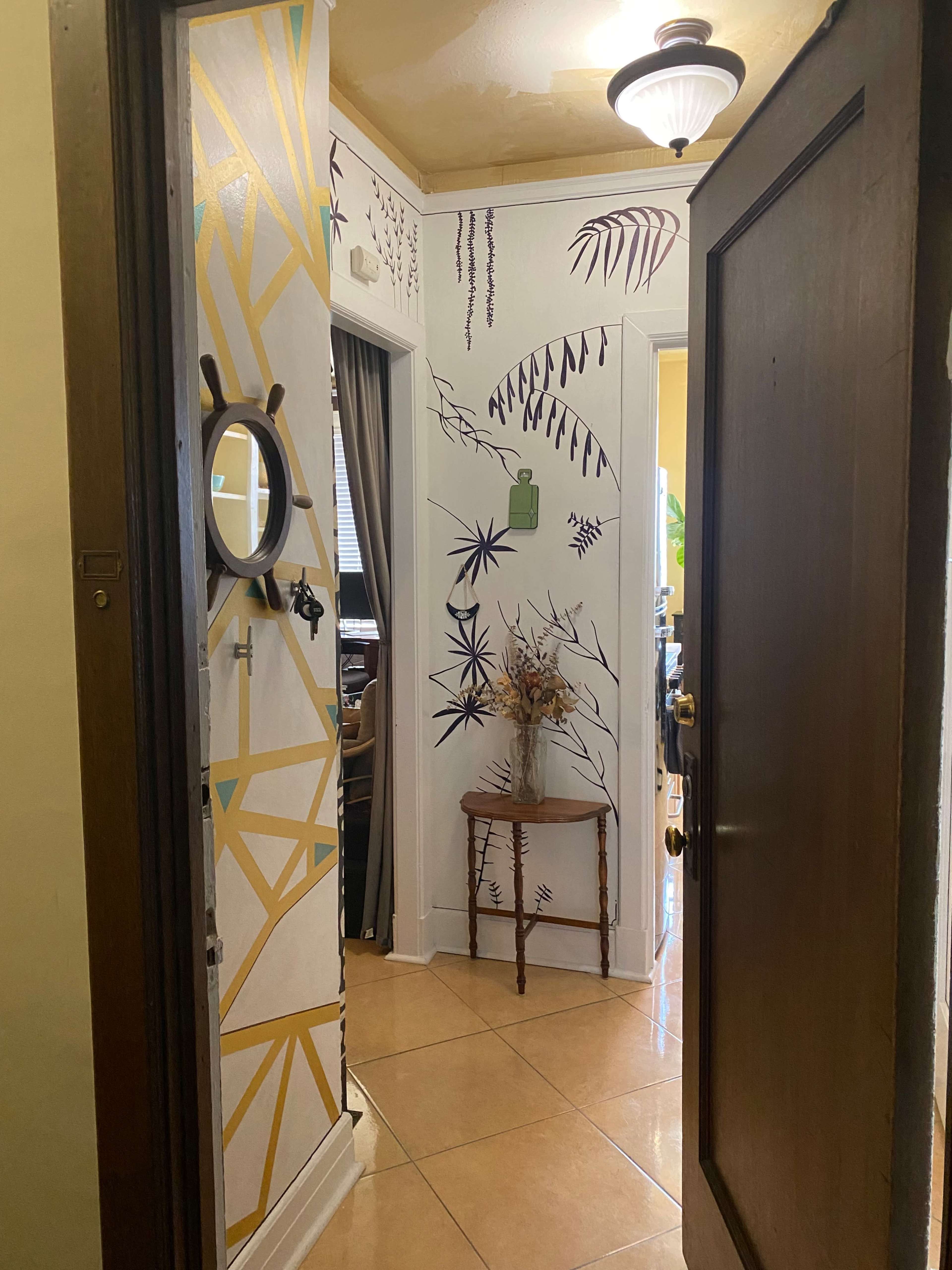 The image shows a hallway with decorative wall designs, a small table with a vase, and doorways leading to adjacent rooms.