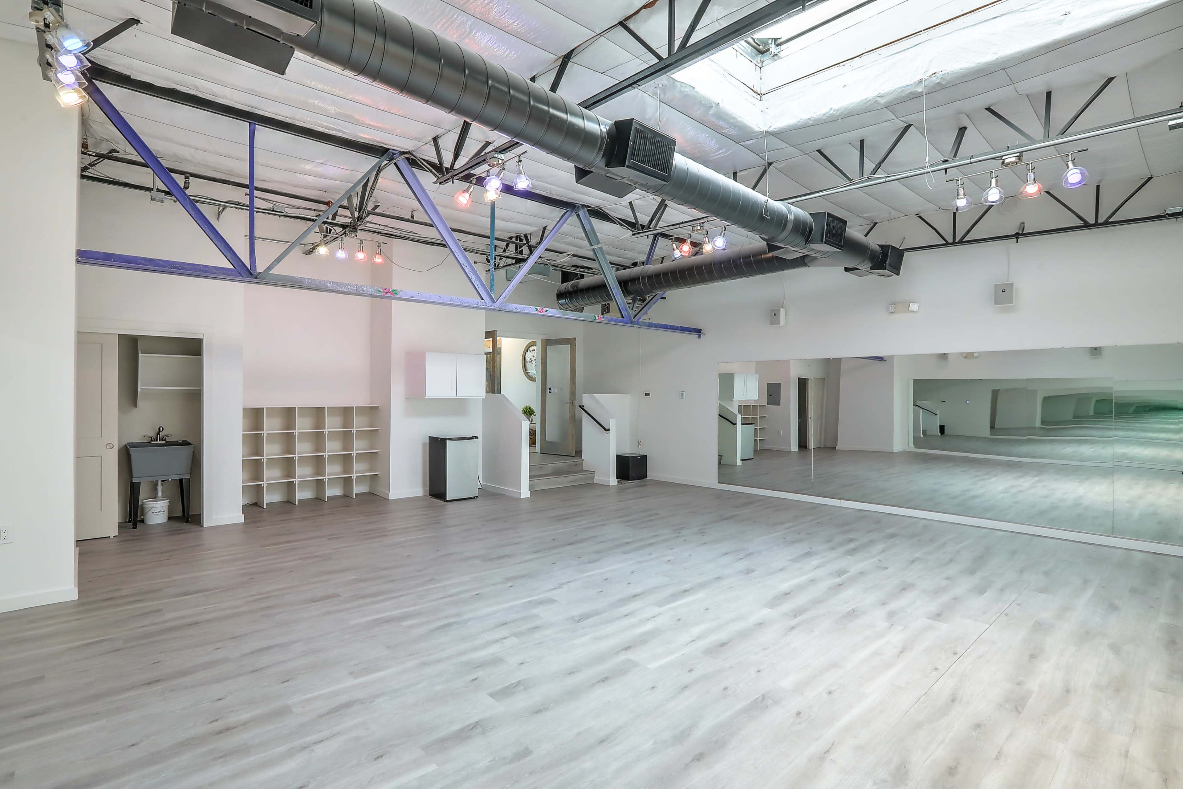 A spacious, well-lit studio with wooden flooring and a large mirror on one wall.
