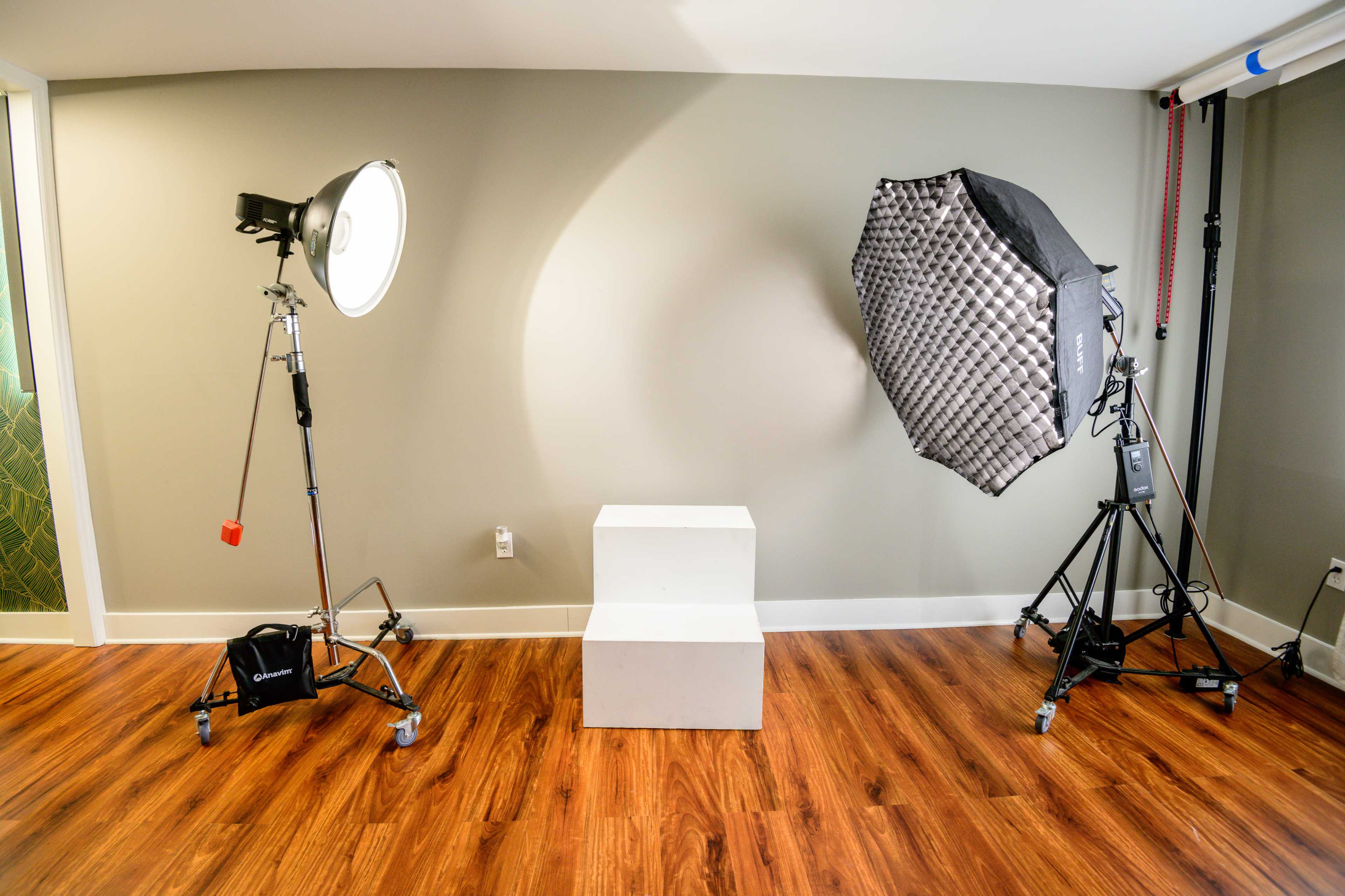 A photography studio setup with two light fixtures positioned on either side of a white pedestal on a wooden floor.