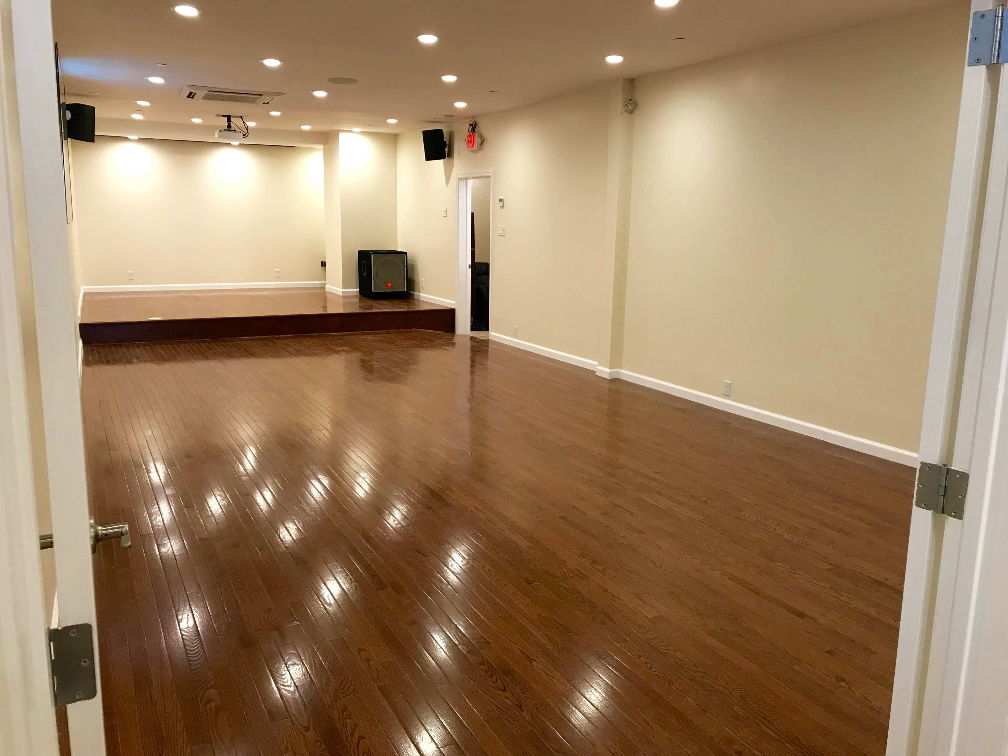 An empty room with polished wooden floors, white walls, and a small stage at the end.